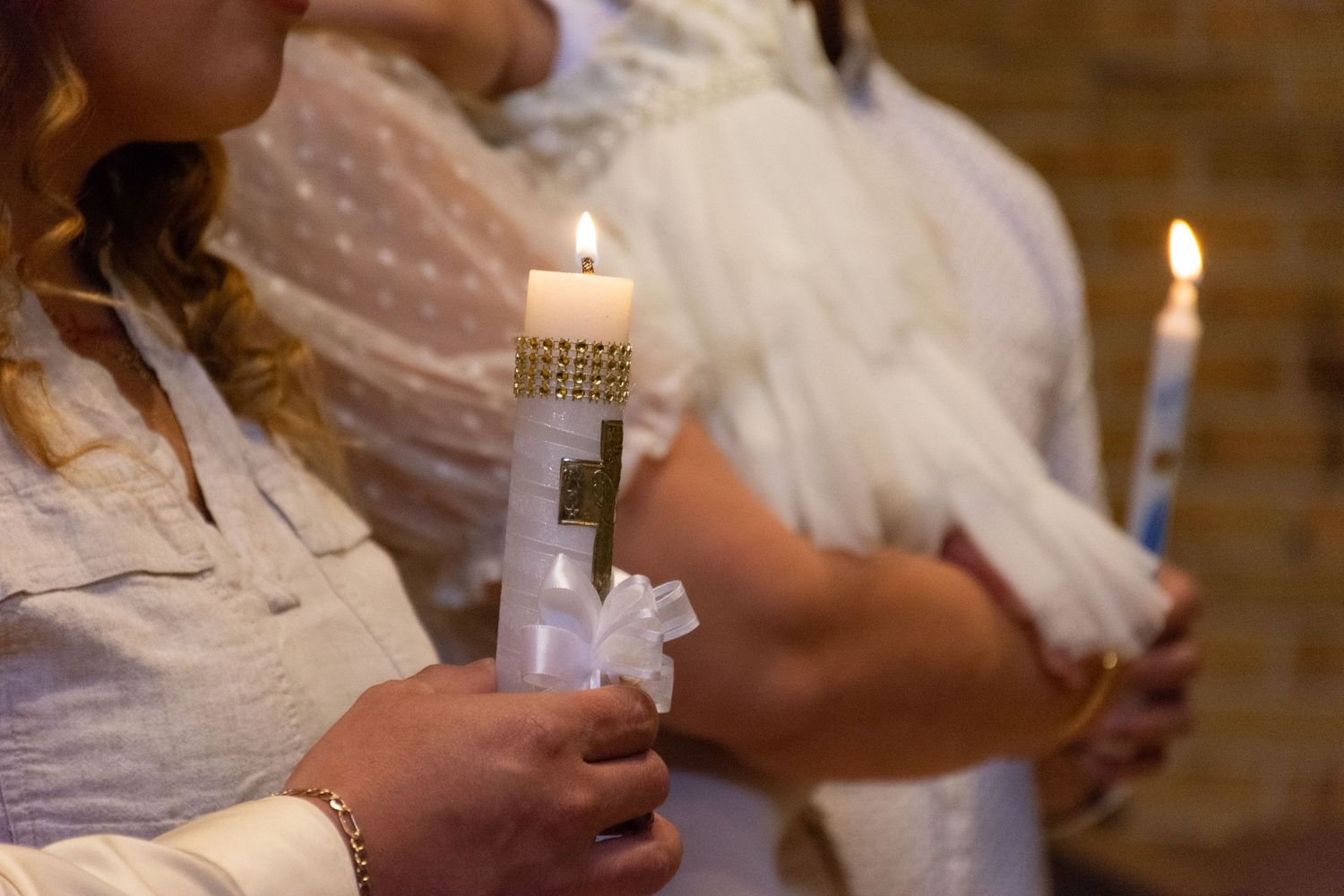 People holding lit candles with white ribbons and cross decorations during a religious ceremony.