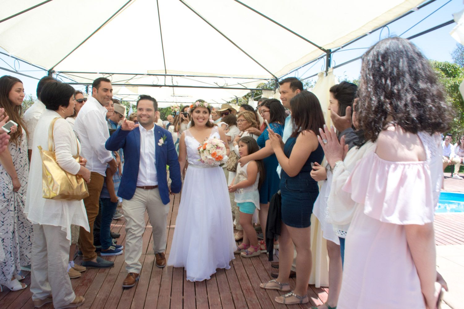 Bride and groom walking through cheering wedding guests under an outdoor canopy.
