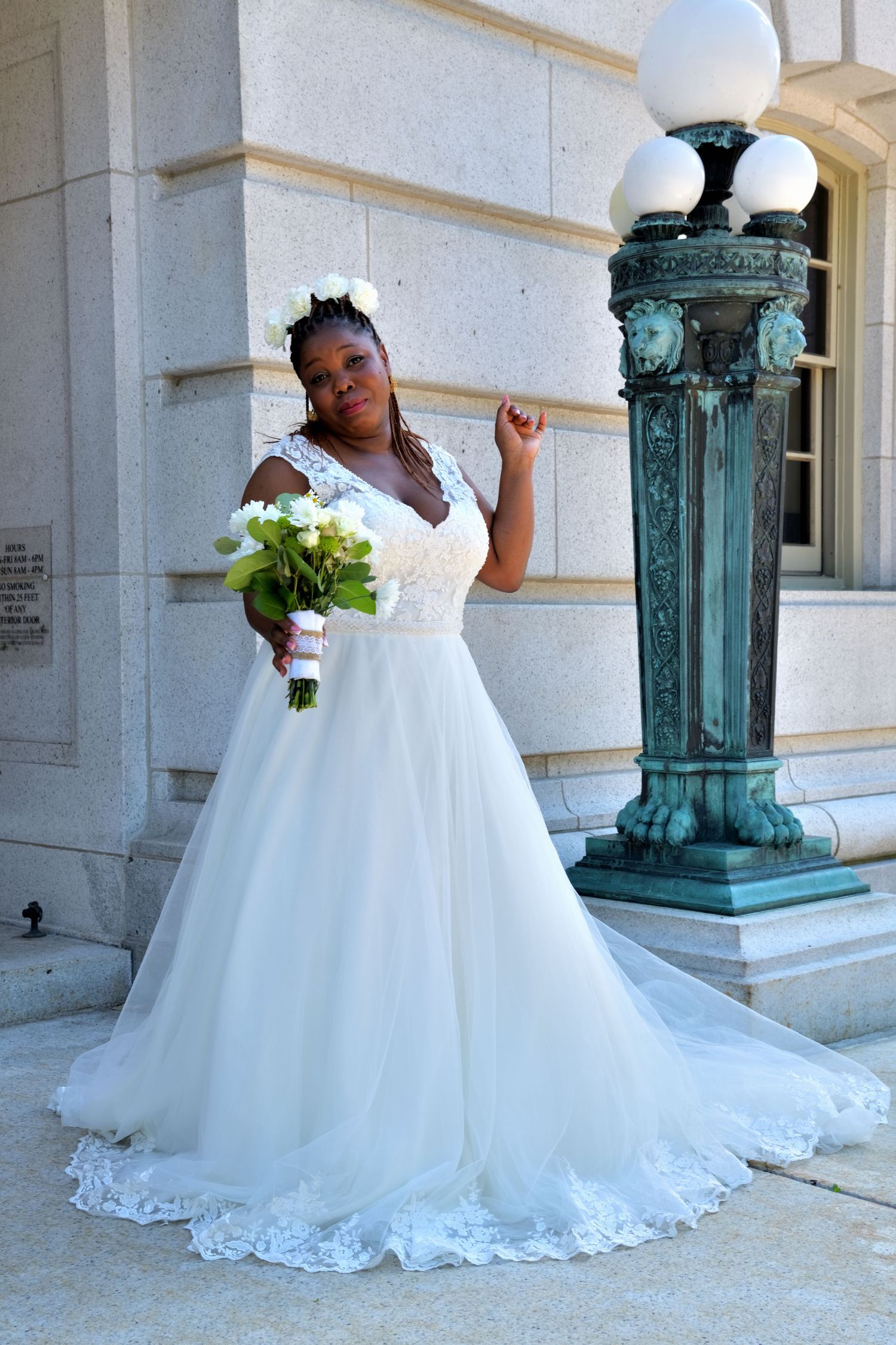 Bride in elegant white ball gown with floral crown poses beside ornate green lamp post.