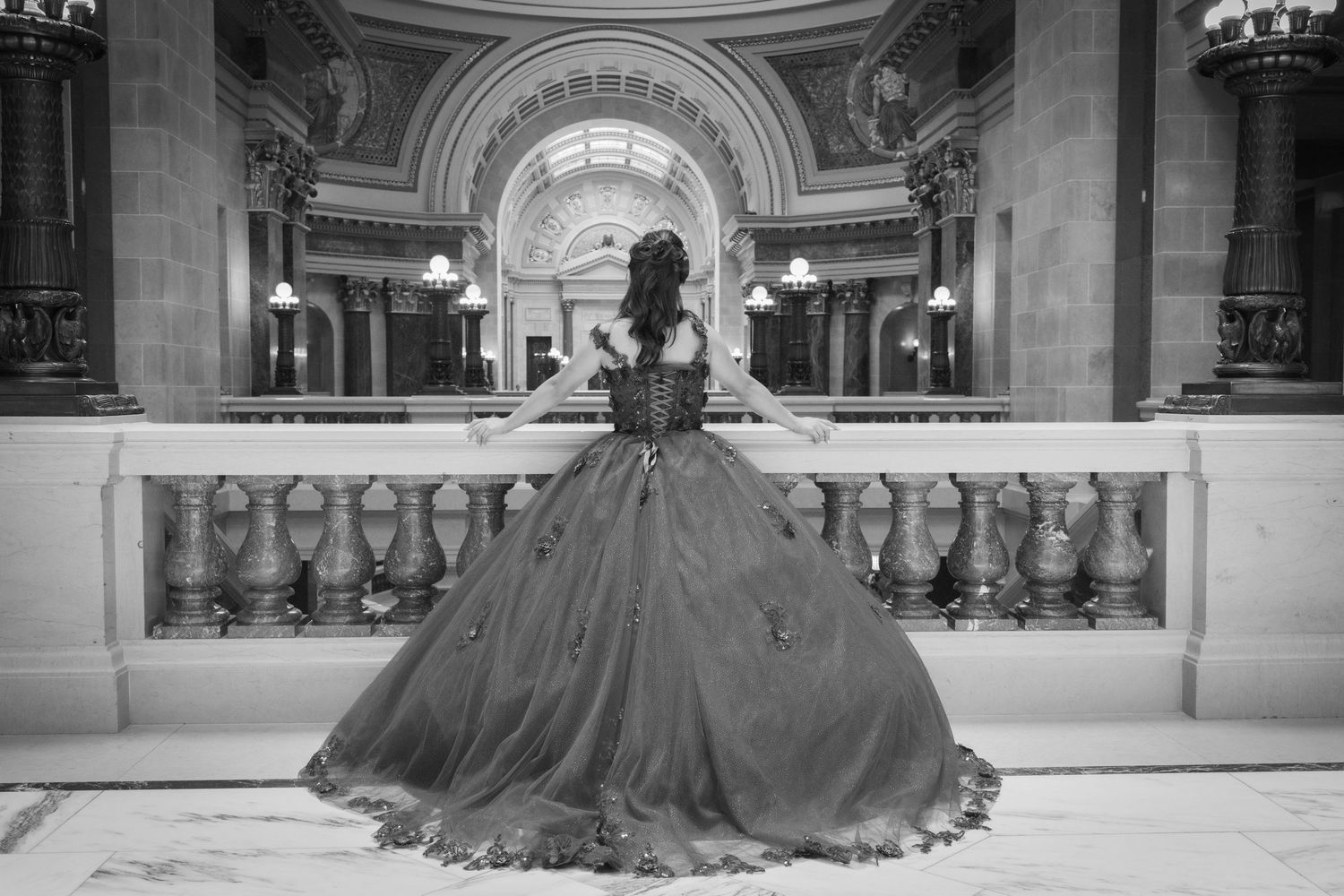 Black and white photo of woman in ball gown overlooking ornate capitol building interior.