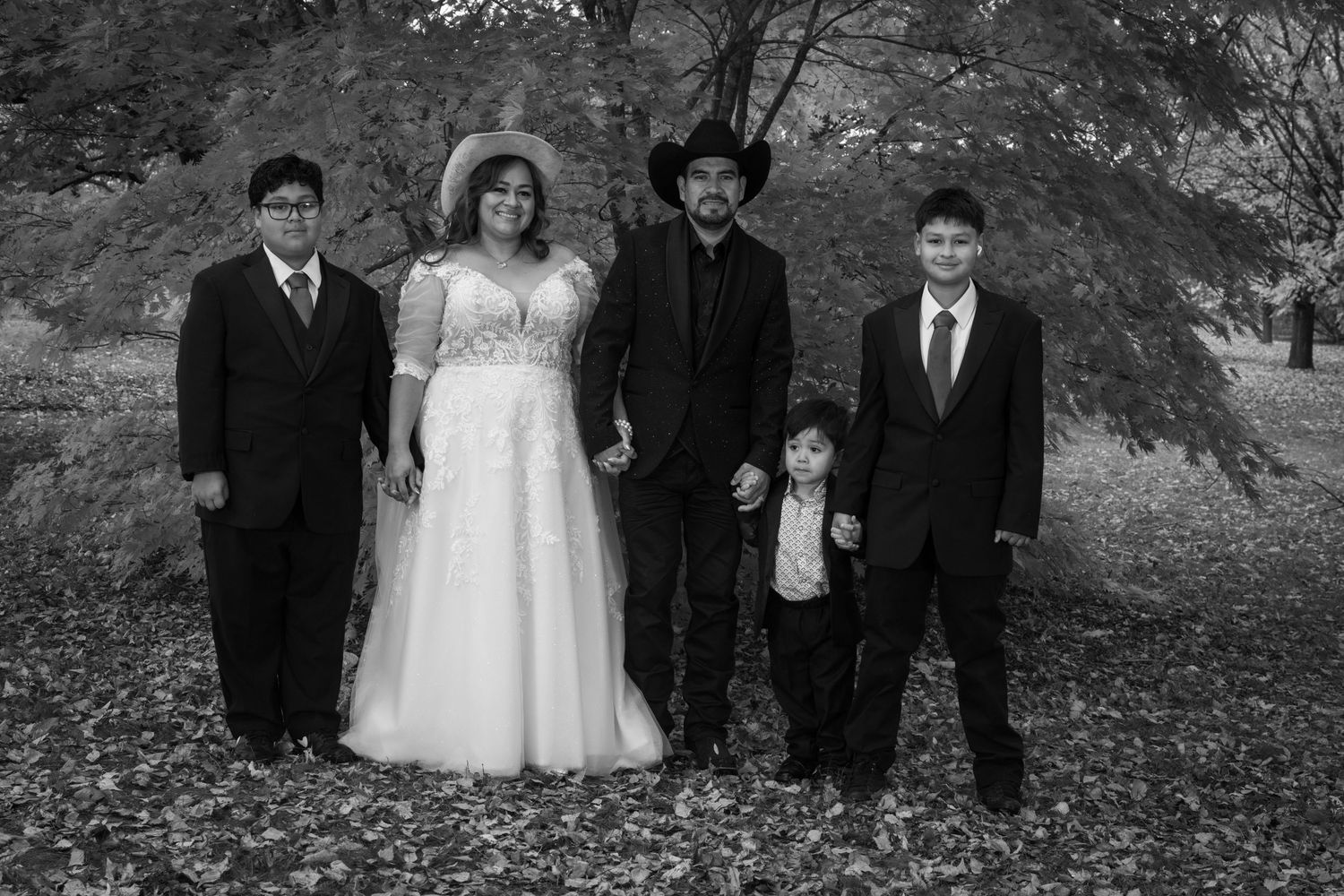 A wedding party of five poses outdoors in black and white, bride in white gown with groom.