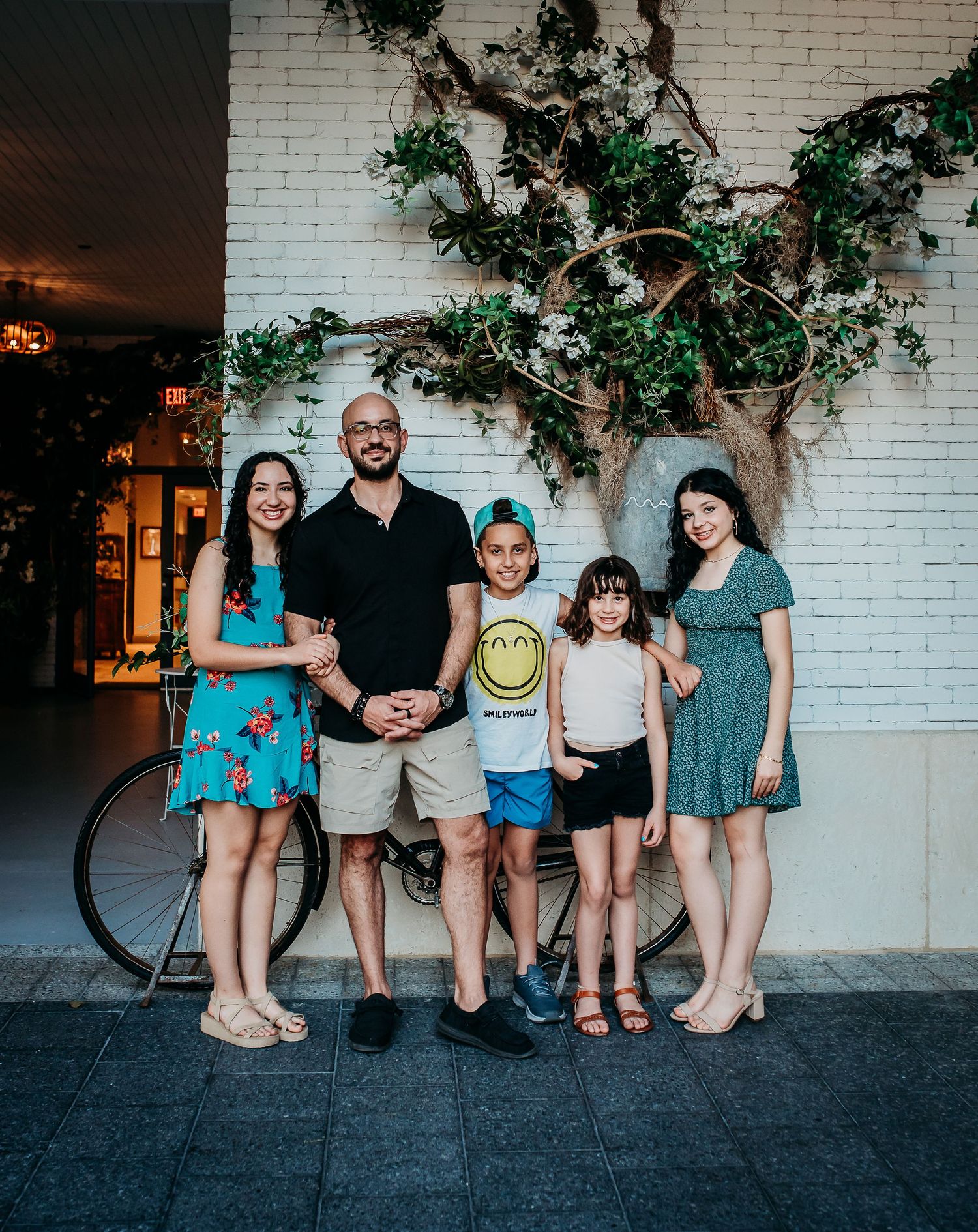 A group stands together in front of a white brick wall with an artistic tree design.