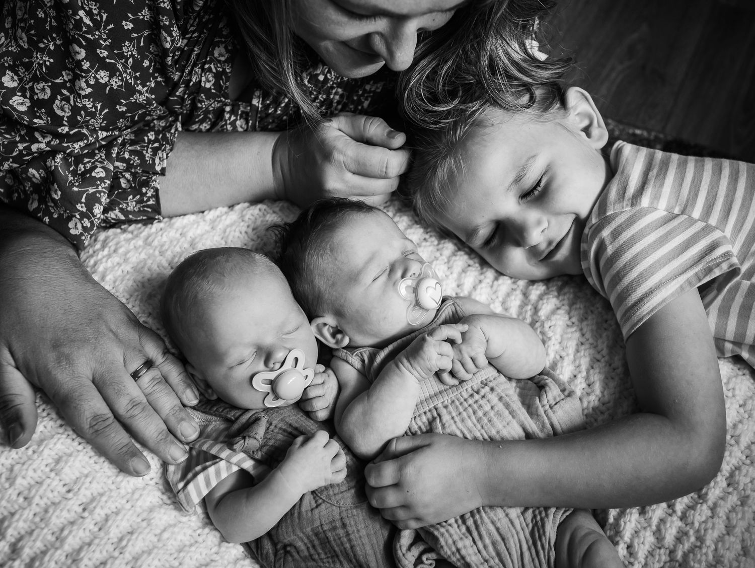 Black and white photograph of siblings sharing a tender moment with their new family member.
