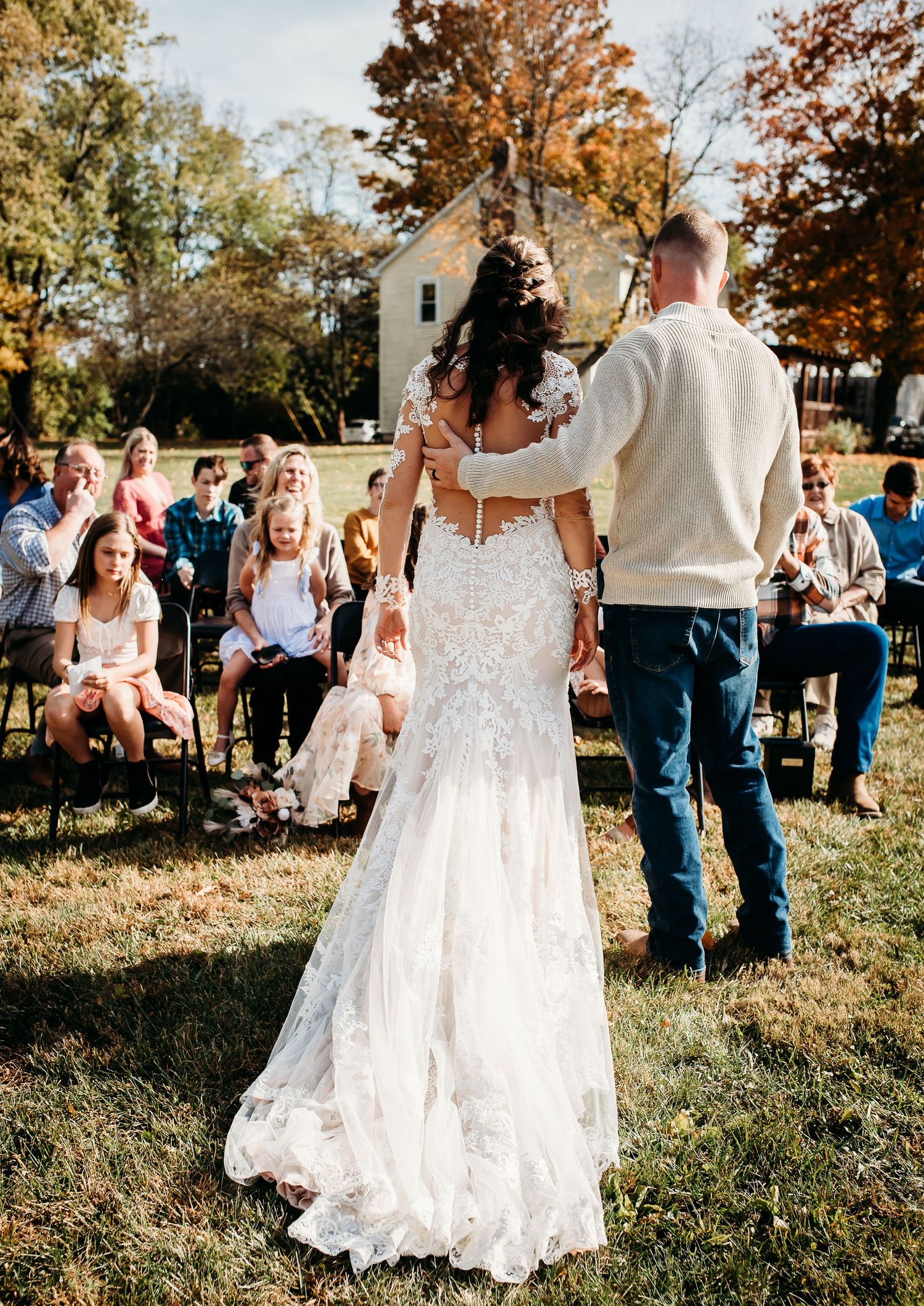 Wedding celebration in an outdoor setting with guests watching as the bride dances in her lace gown.