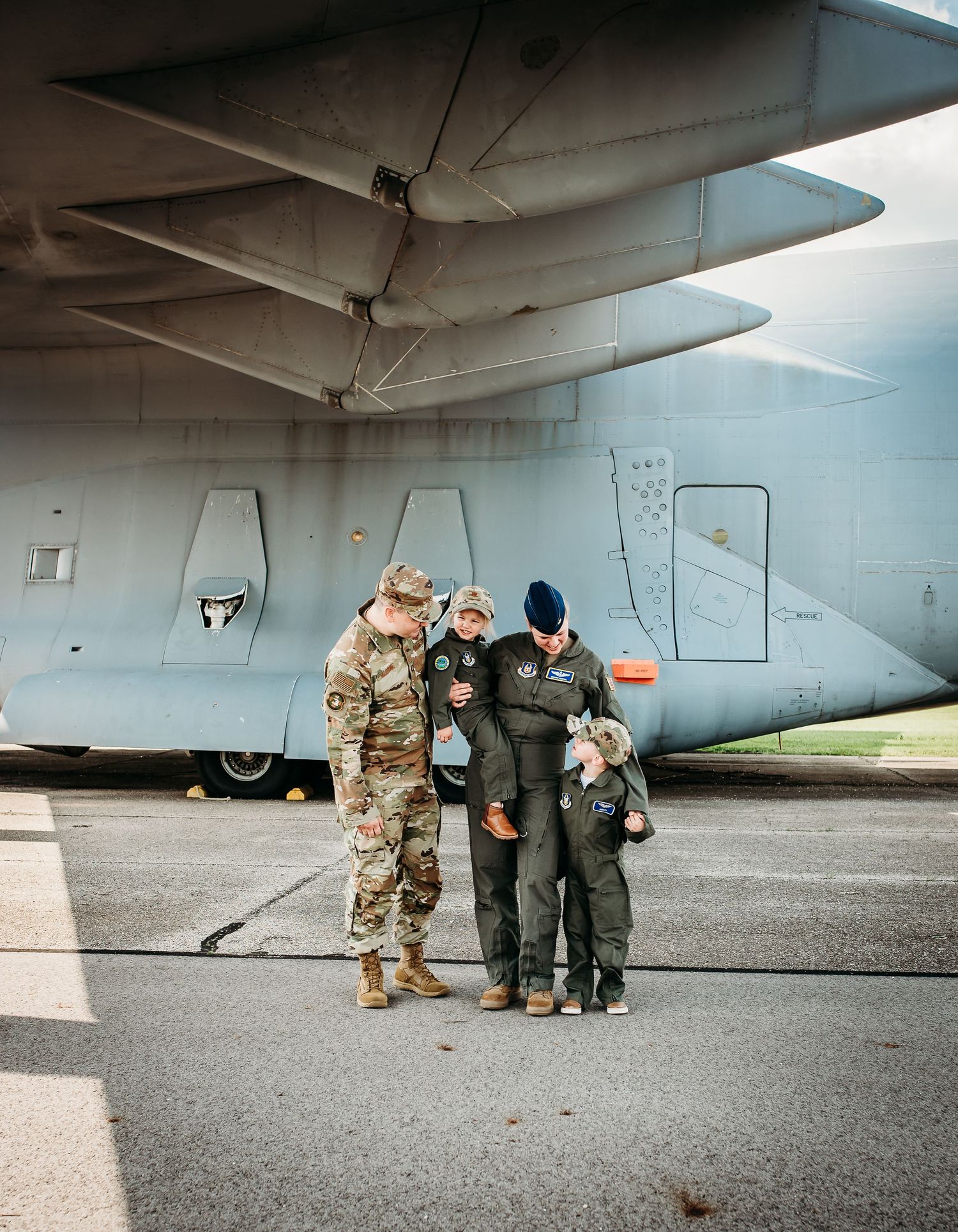Group poses under the wing of a military aircraft for a photo.