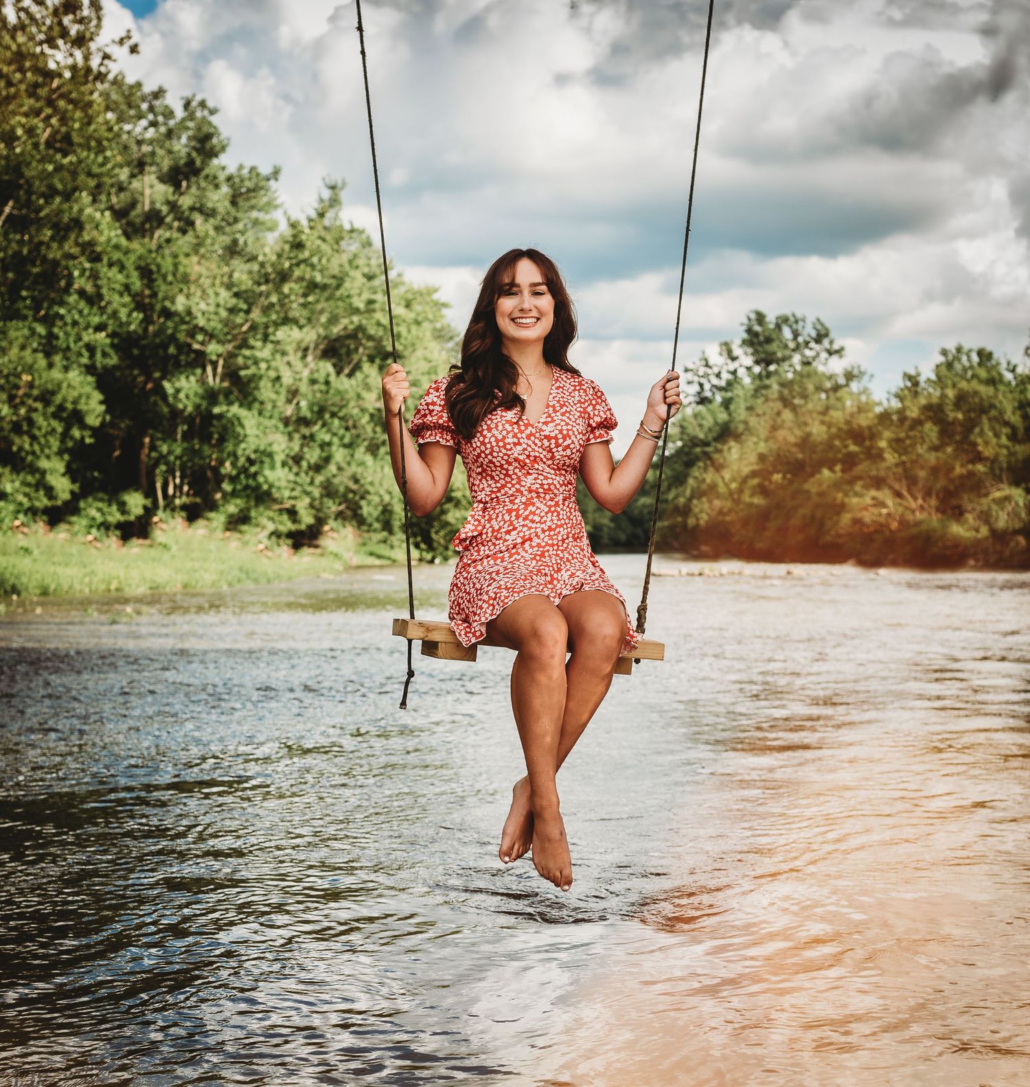 Woman in red dress swinging joyfully over tranquil water on a summer day.