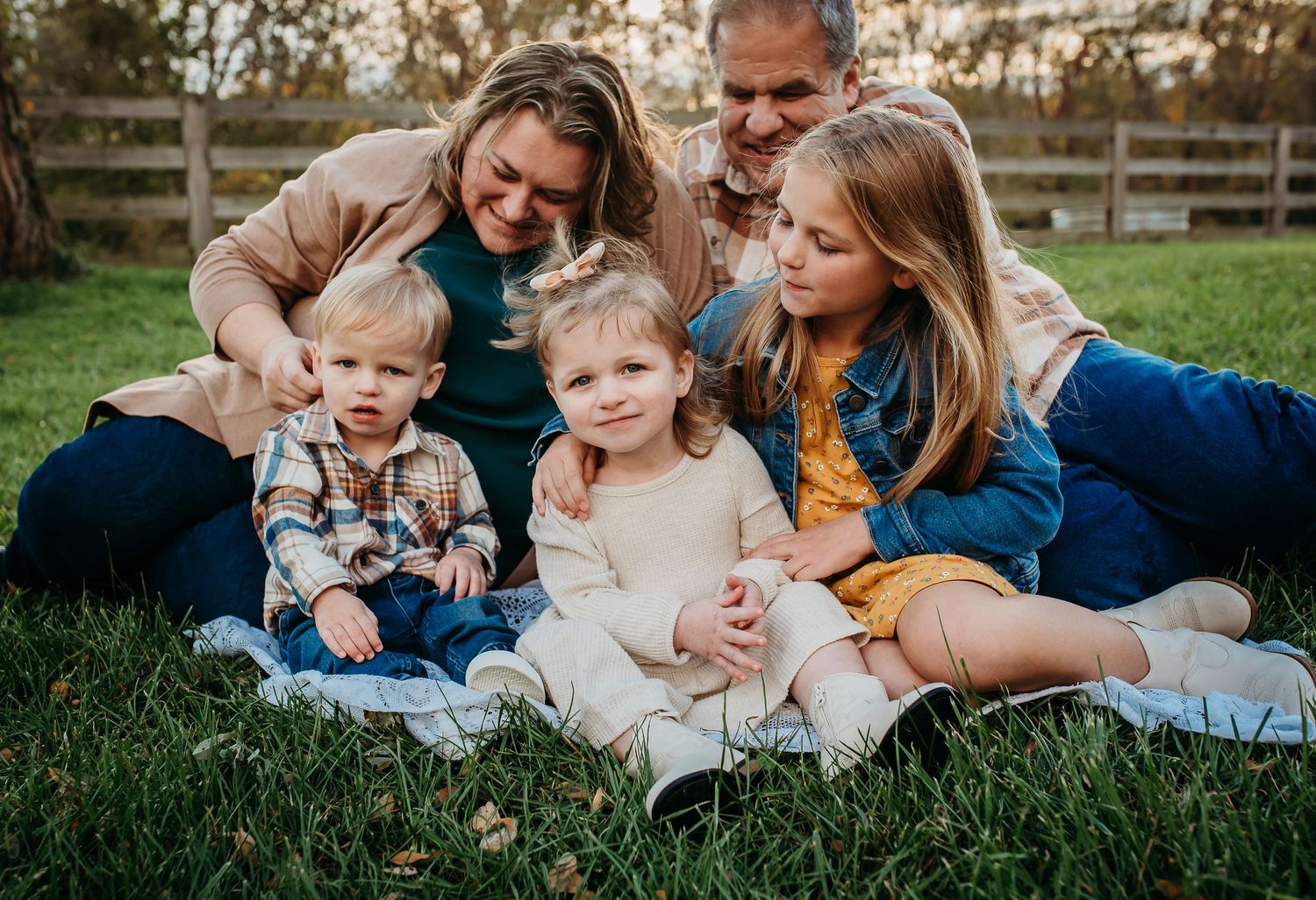 A family group shares a candid moment while sitting on a blanket in a grassy field.