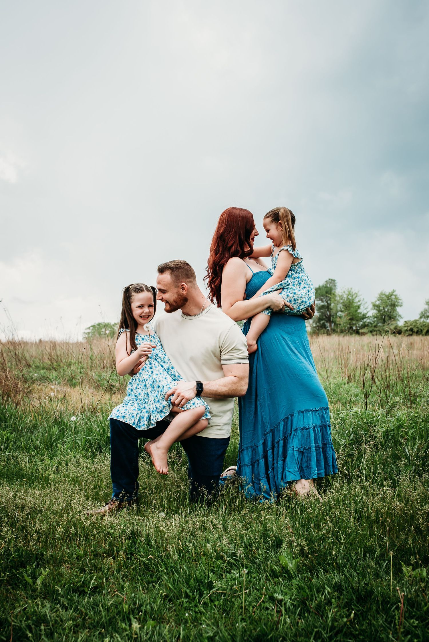 A family poses together in a meadow wearing coordinated blue and white outfits.