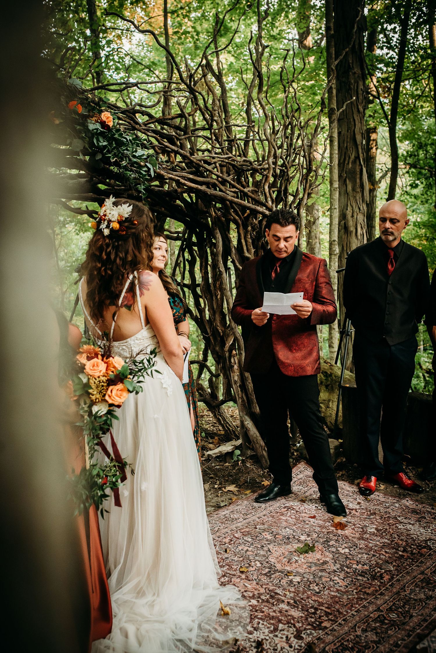 Intimate woodland wedding ceremony taking place under twisted branch archway.