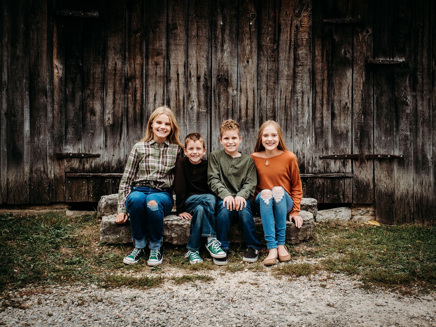 A rustic family portrait in front of a weathered wooden barn wall with everyone sitting casually on stone steps.