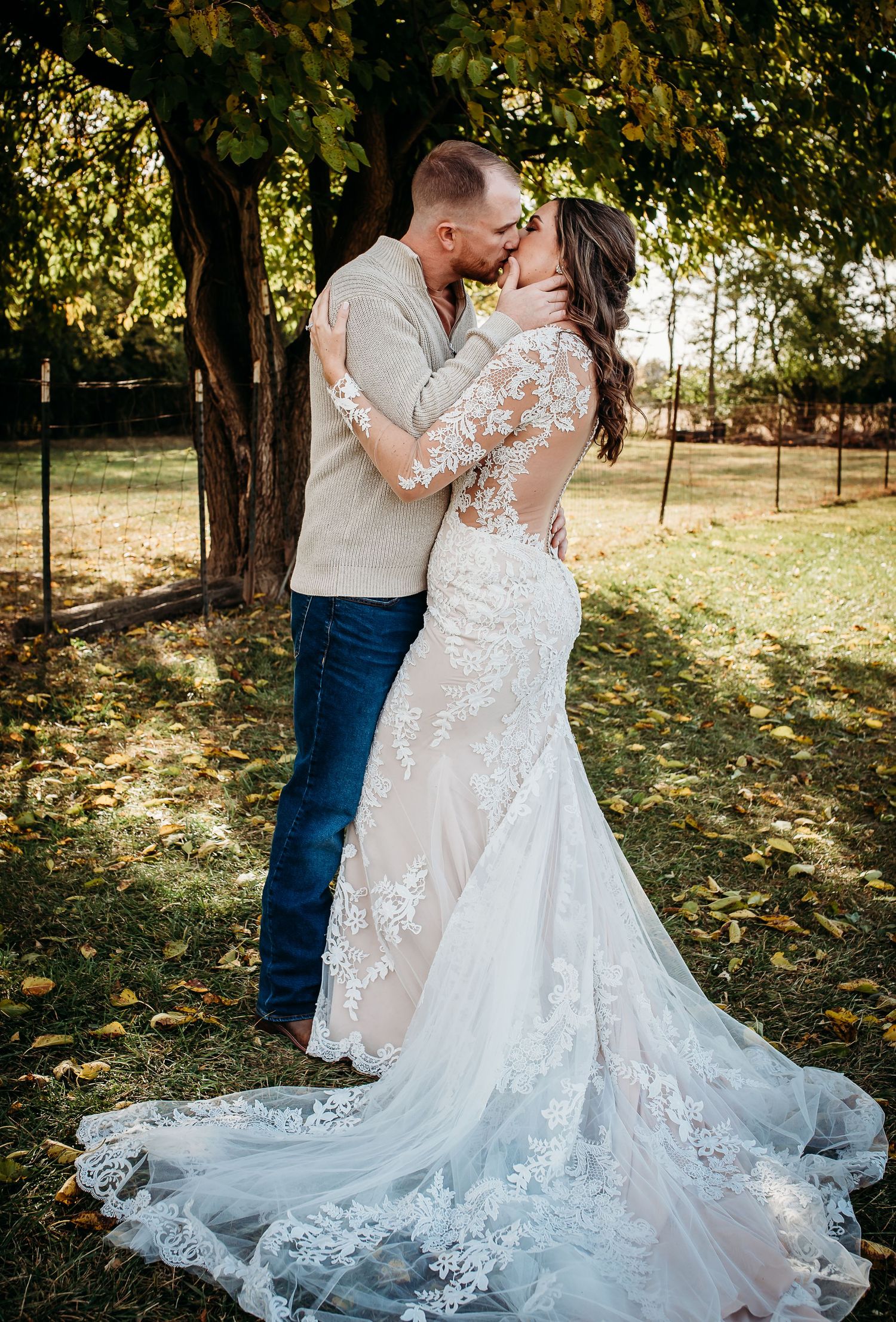 Elegant white lace wedding gown flowing across ground in outdoor autumn setting.