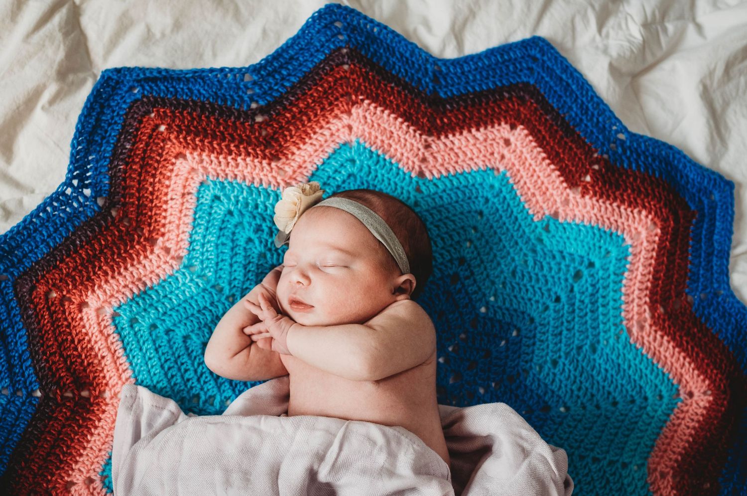 Sleeping newborn on striped blue, coral and turquoise crochet blanket.
