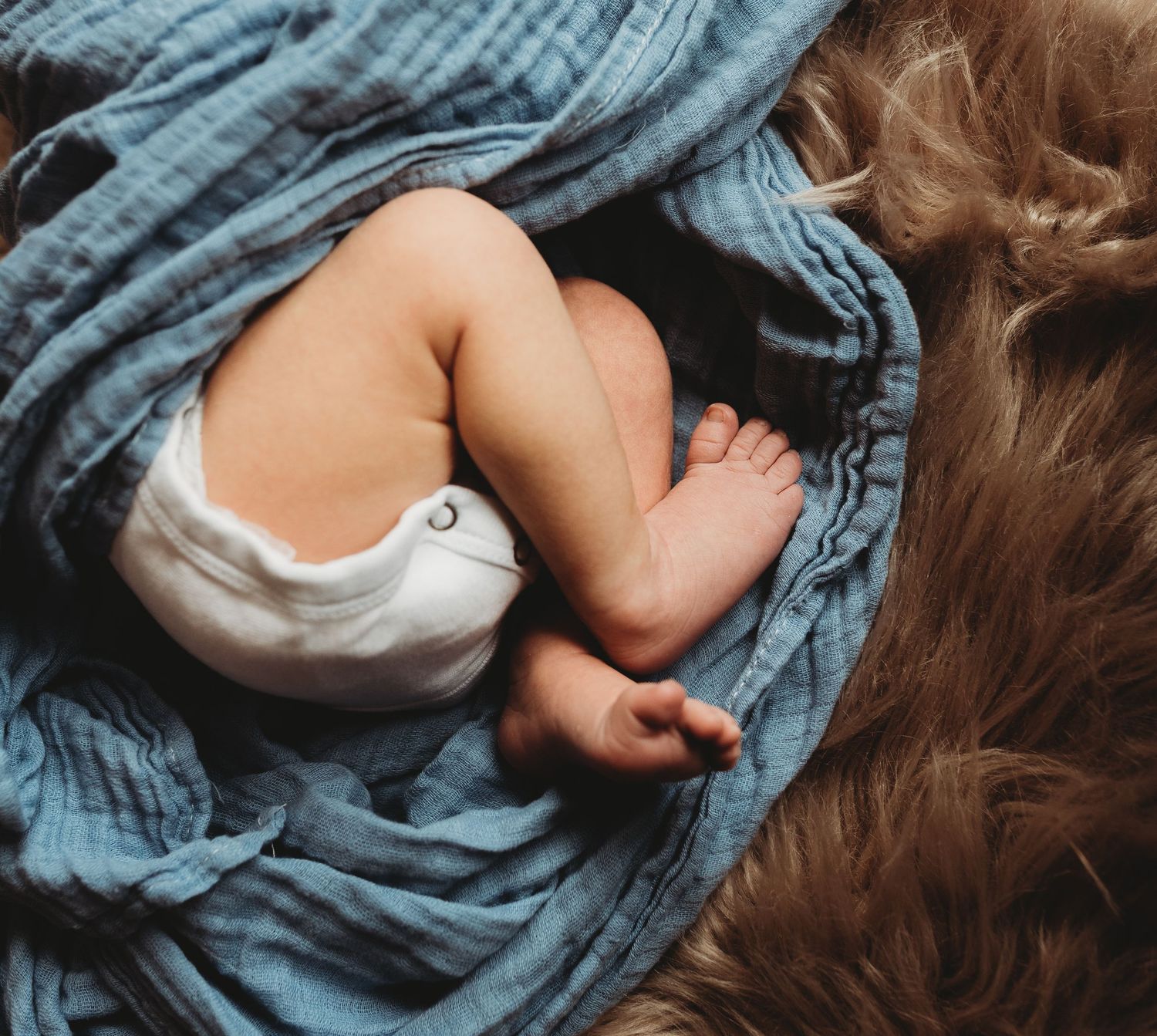 Close-up of tiny baby feet against blue textile and soft fur.