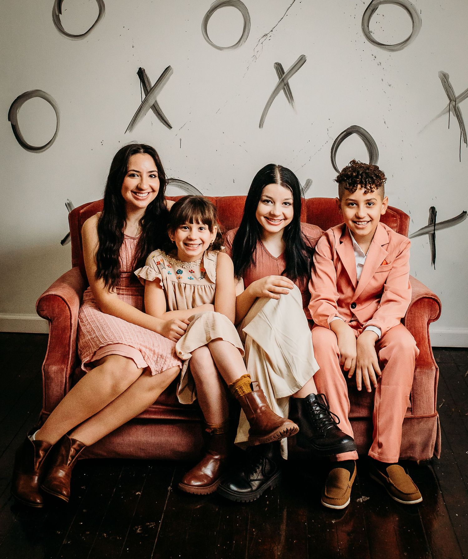 A family group poses together on red vintage couch against wall with tic-tac-toe pattern.