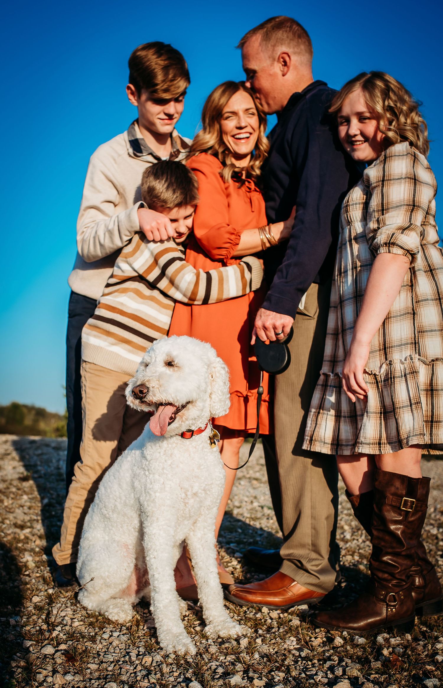 A joyful family portrait with white dog outdoors against vivid blue sky.