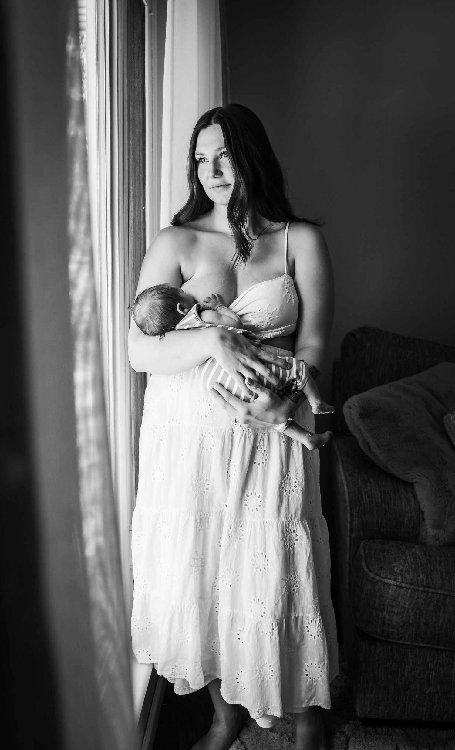 A black and white portrait of a nurturing moment beside a window in soft natural light.