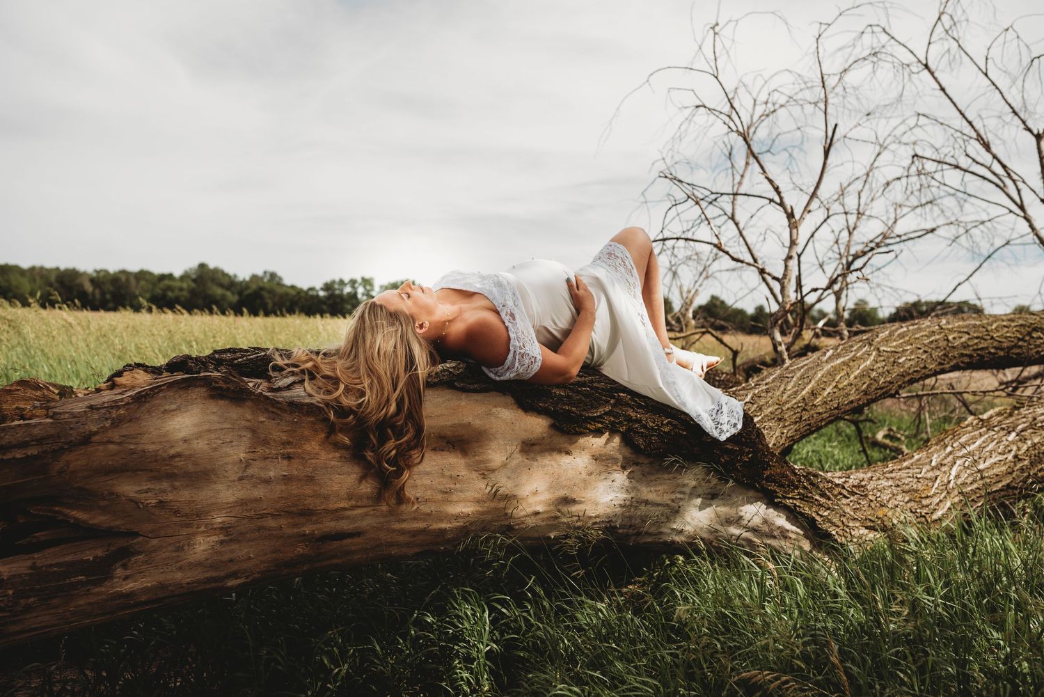 A person lying peacefully on a large fallen tree trunk in a sunlit meadow.