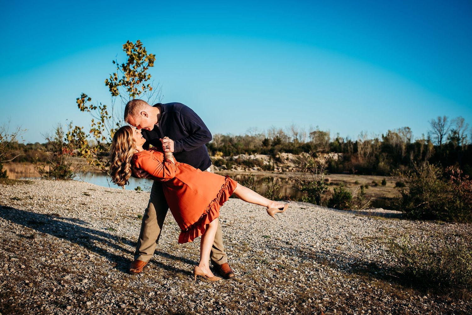 A romantic dip pose between couple on rocky terrain against bright blue sky.