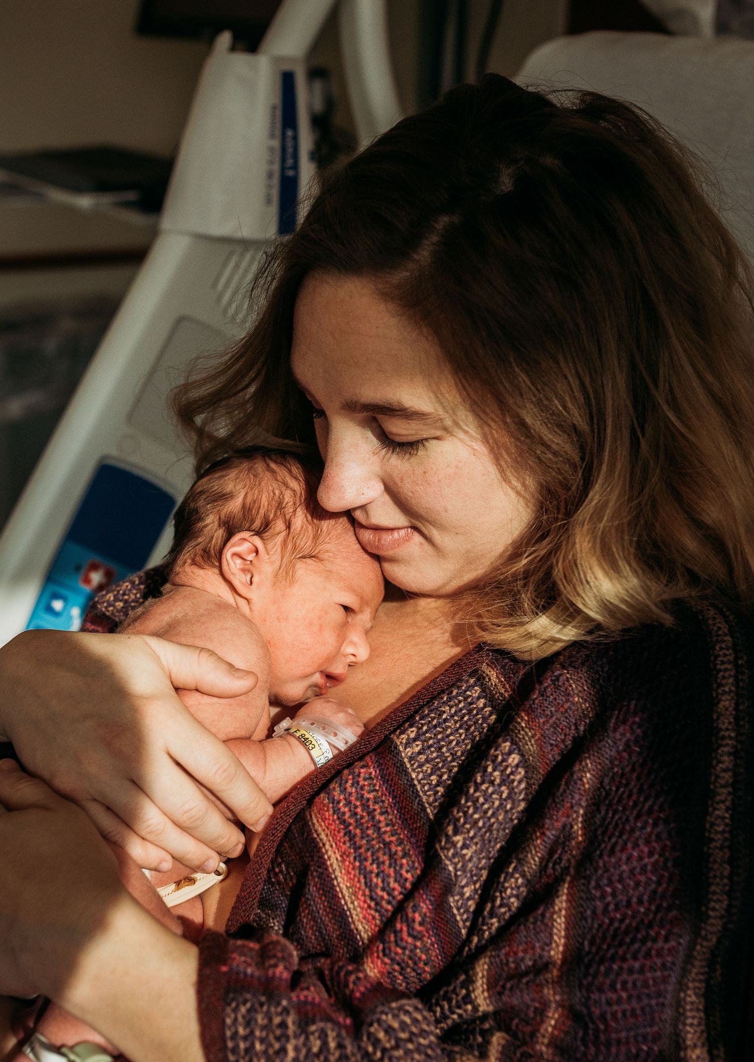 A tender moment between mother and newborn in soft window light.