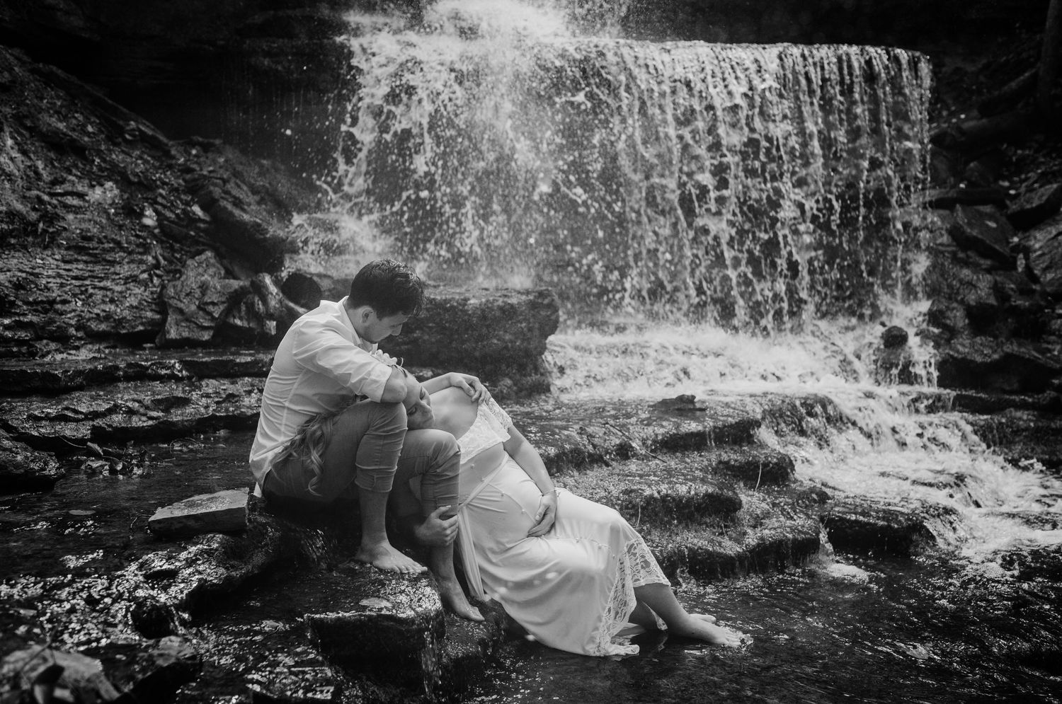 A romantic black and white photo of a couple relaxing by a cascading waterfall.