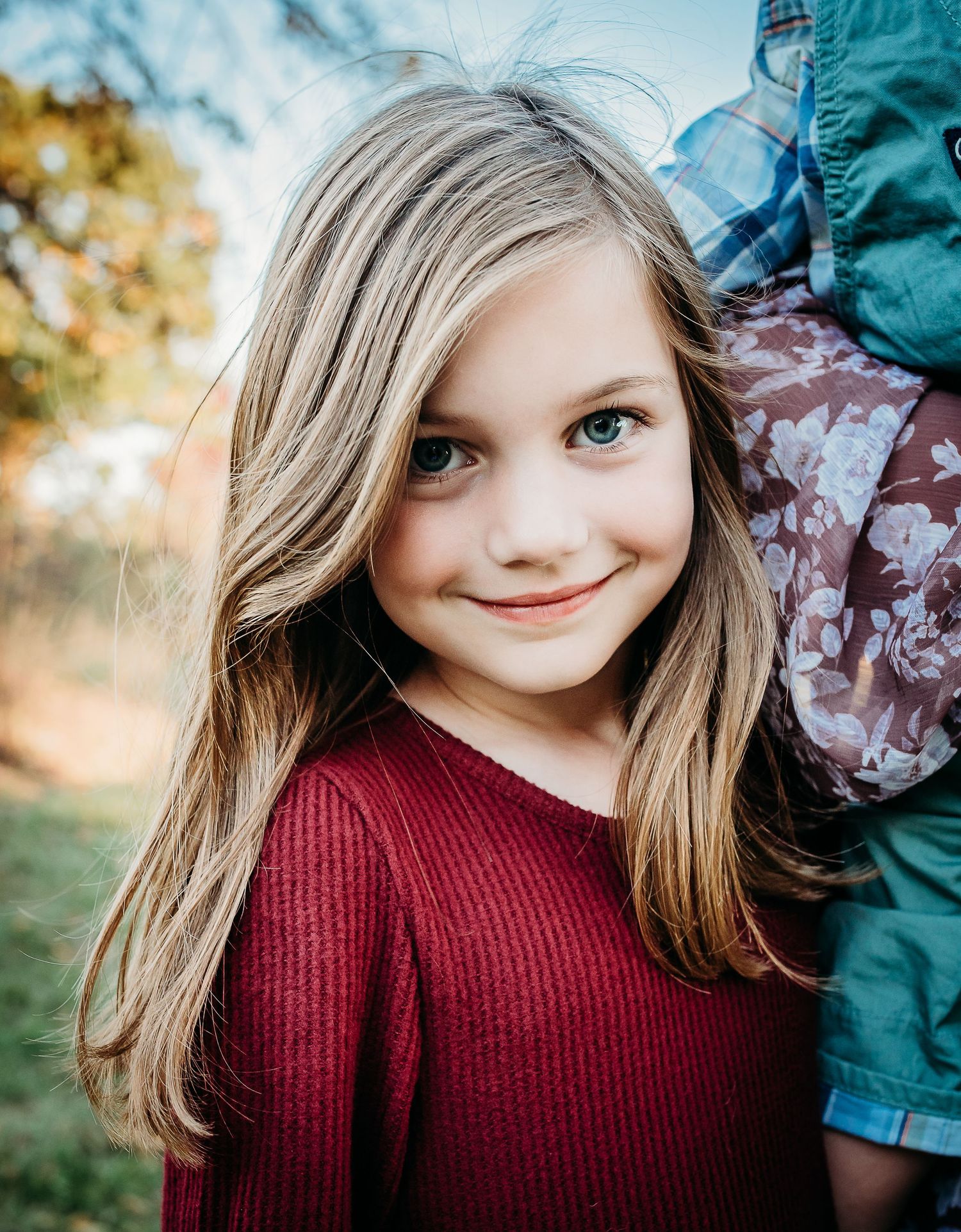 Portrait of someone wearing a burgundy sweater with long hair against an autumn background.