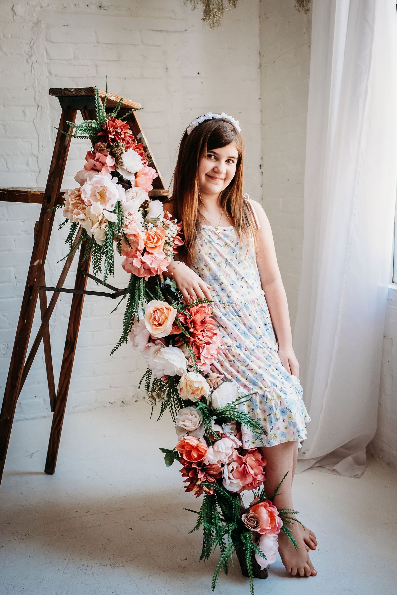 Someone in a floral dress poses near wooden ladders decorated with pink and coral flowers.