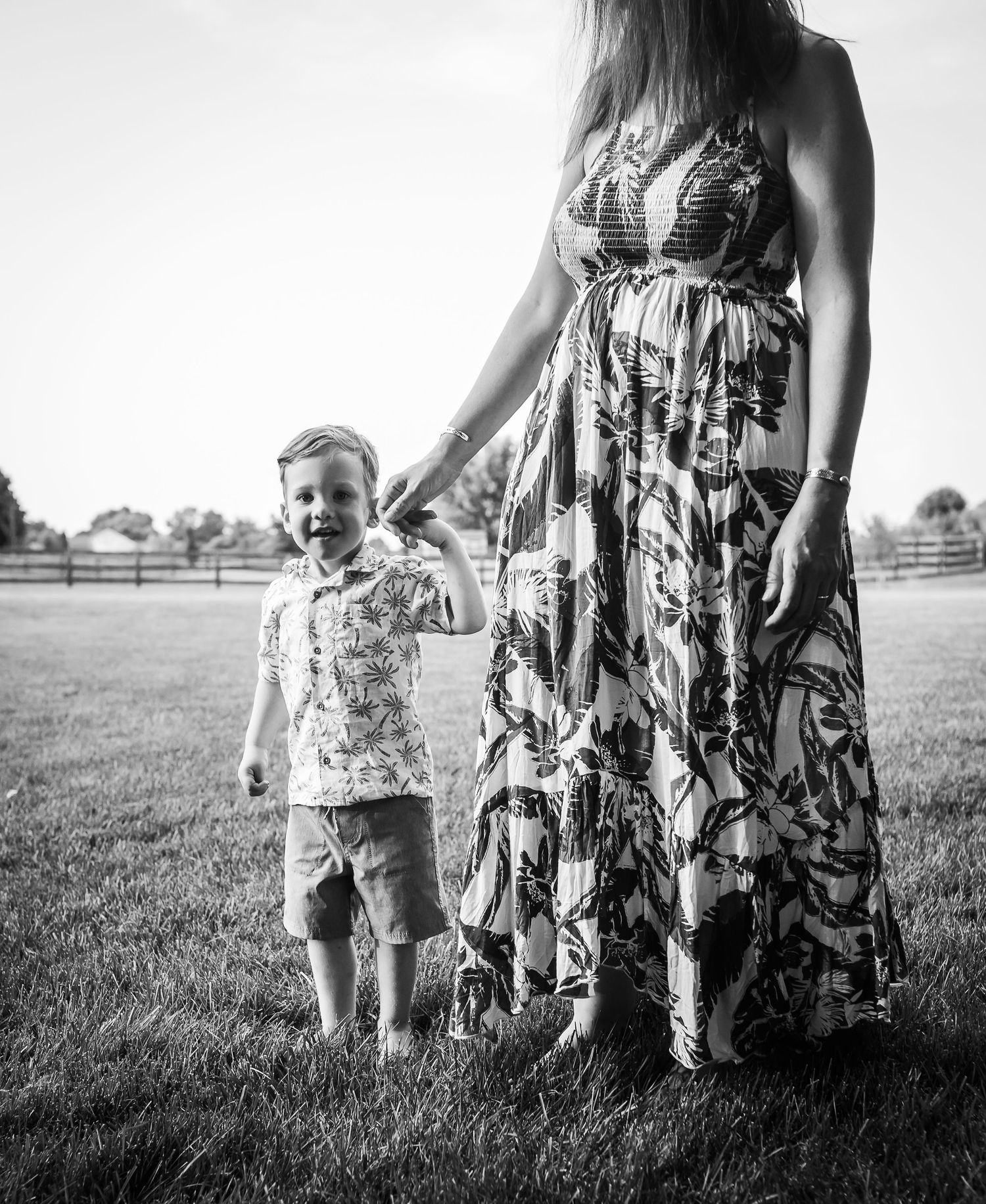 A black and white portrait of two people standing in a grassy field with a fence in the background.