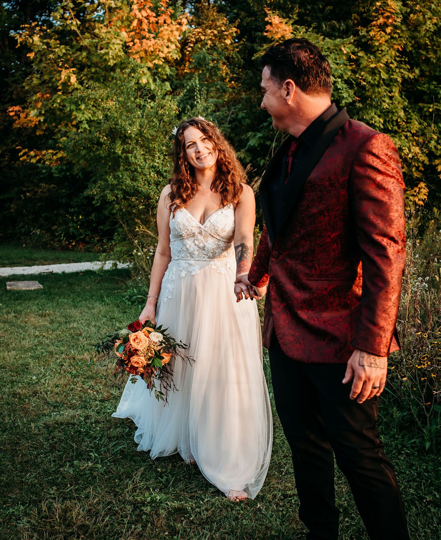 Couple shares romantic moment in autumn garden setting with white dress and burgundy suit.