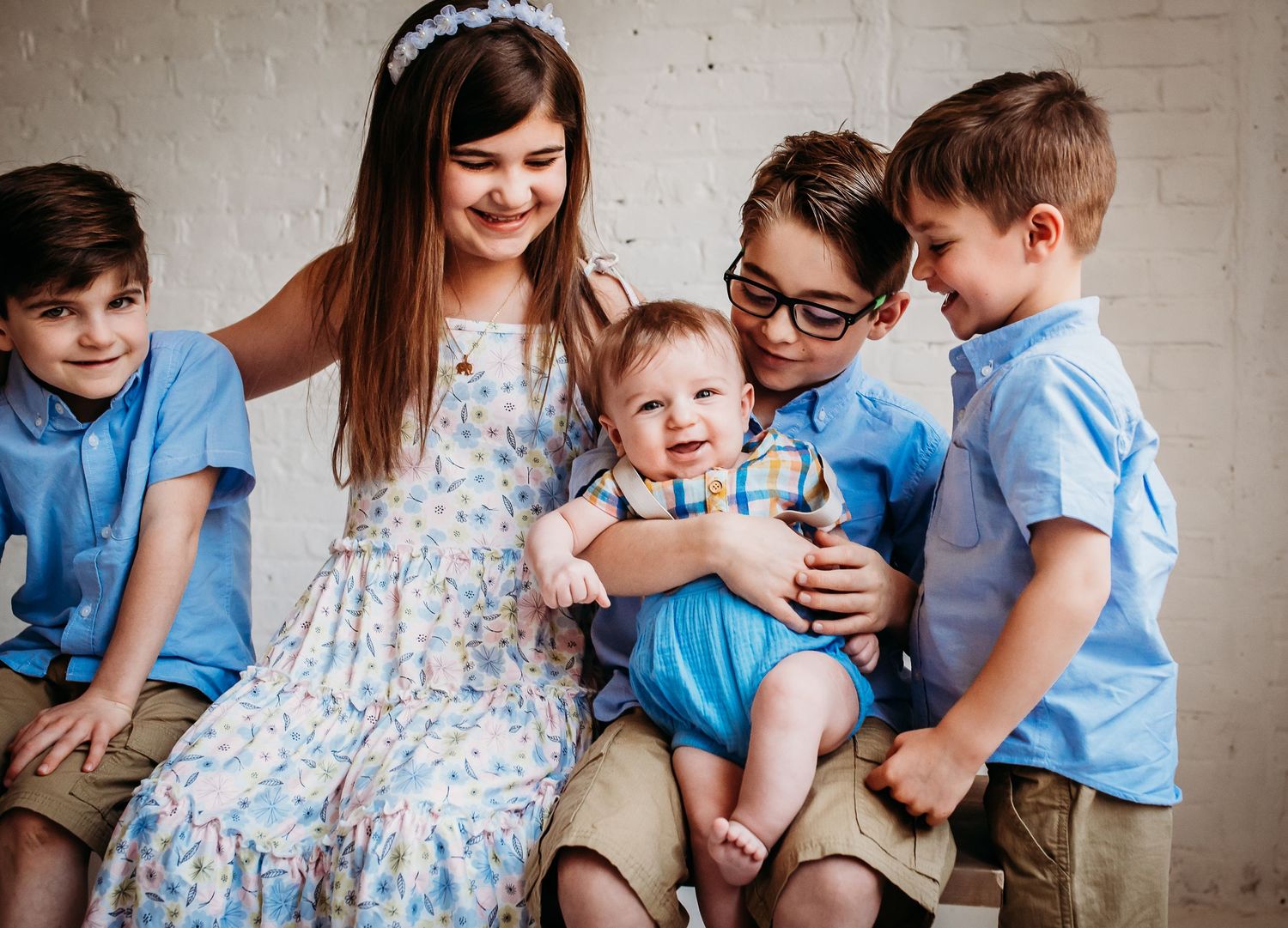 A family wearing coordinating blue outfits sits together against a white brick wall.