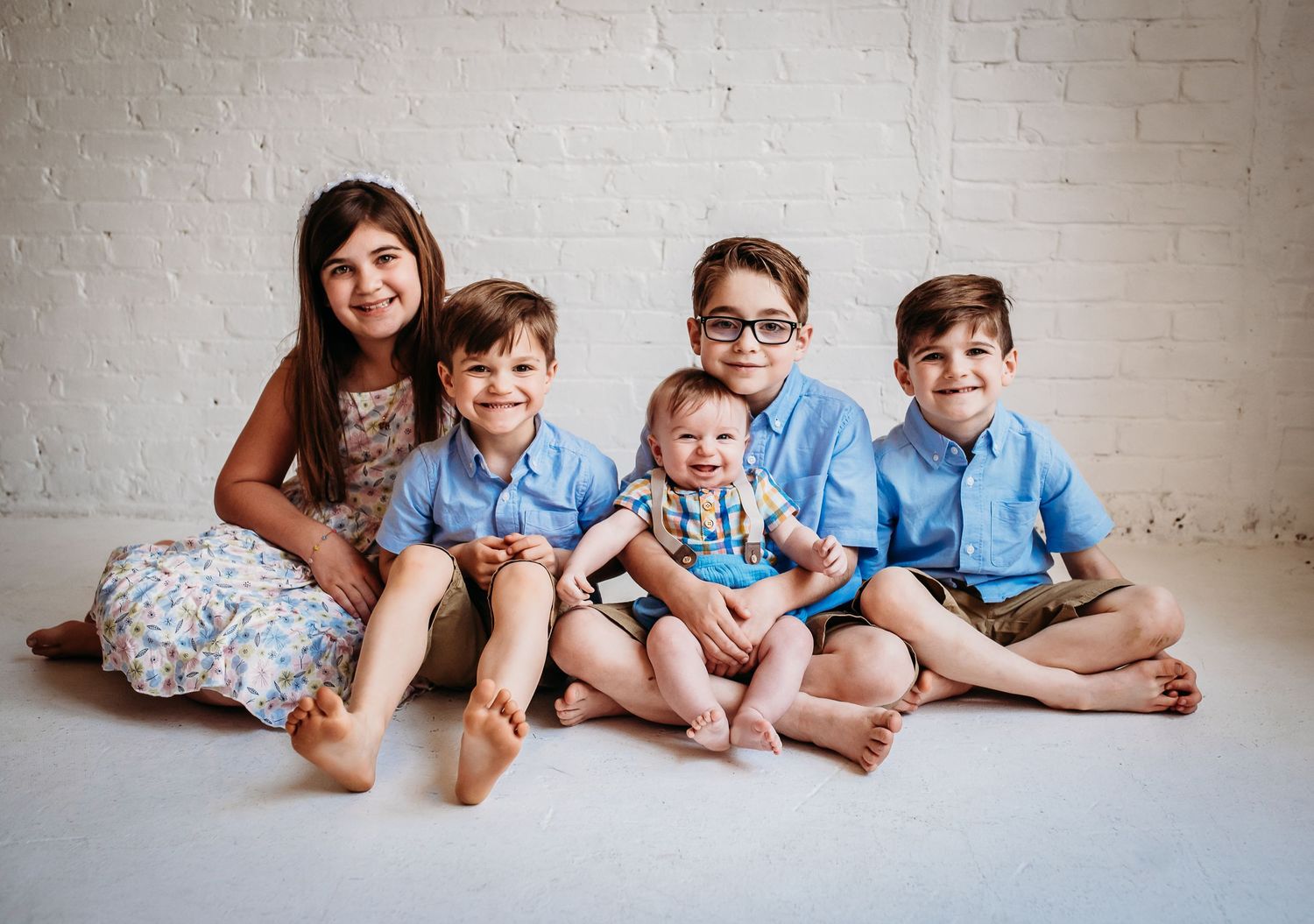 A family group in matching blue shirts sits together on a white floor against a brick wall.