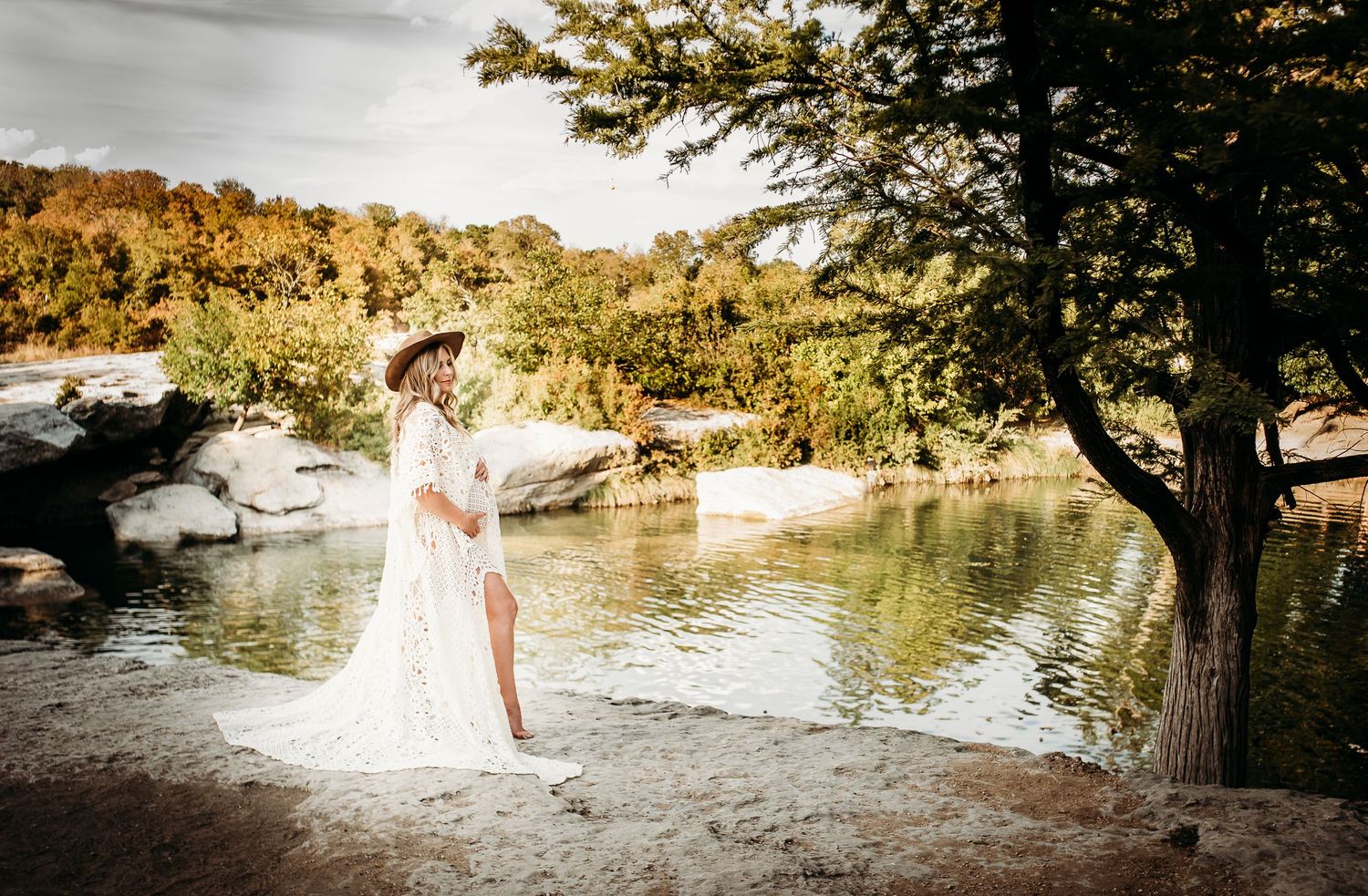 A romantic bridal portrait by a scenic river with autumn foliage and rocks in the background.