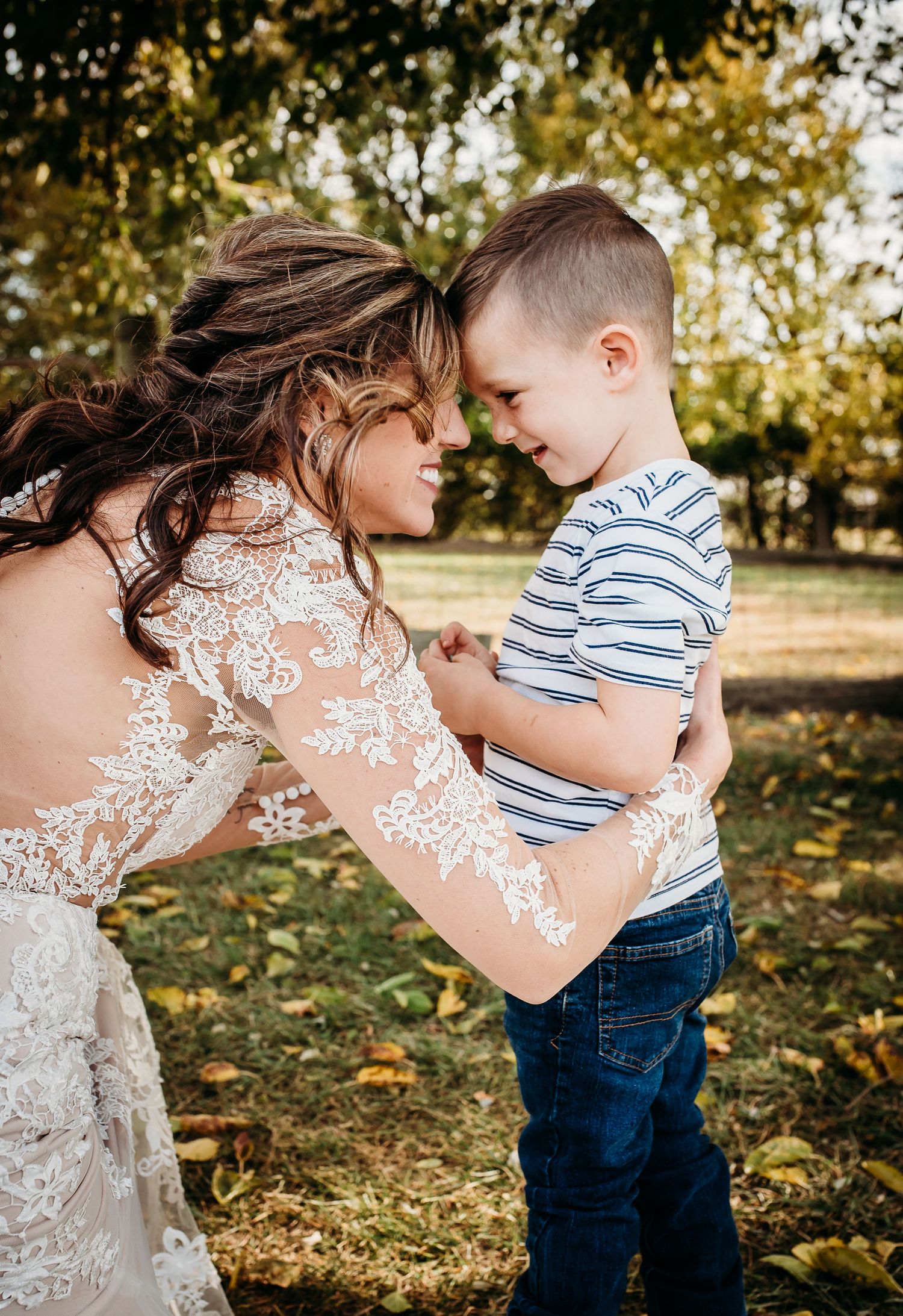 Tender moment between someone in a lace wedding dress and a small child in striped shirt and jeans.