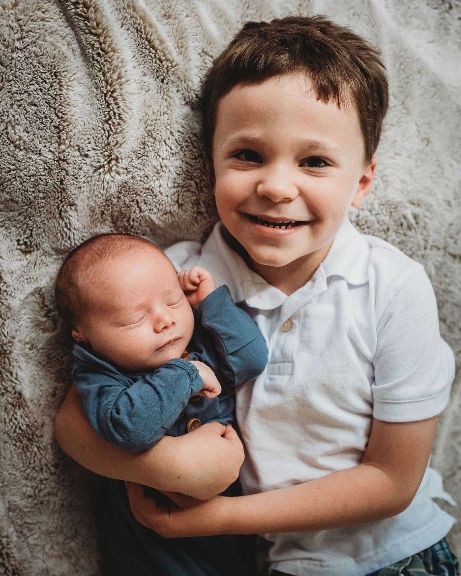 Sweet siblings cuddling together on textured carpet during photo session.