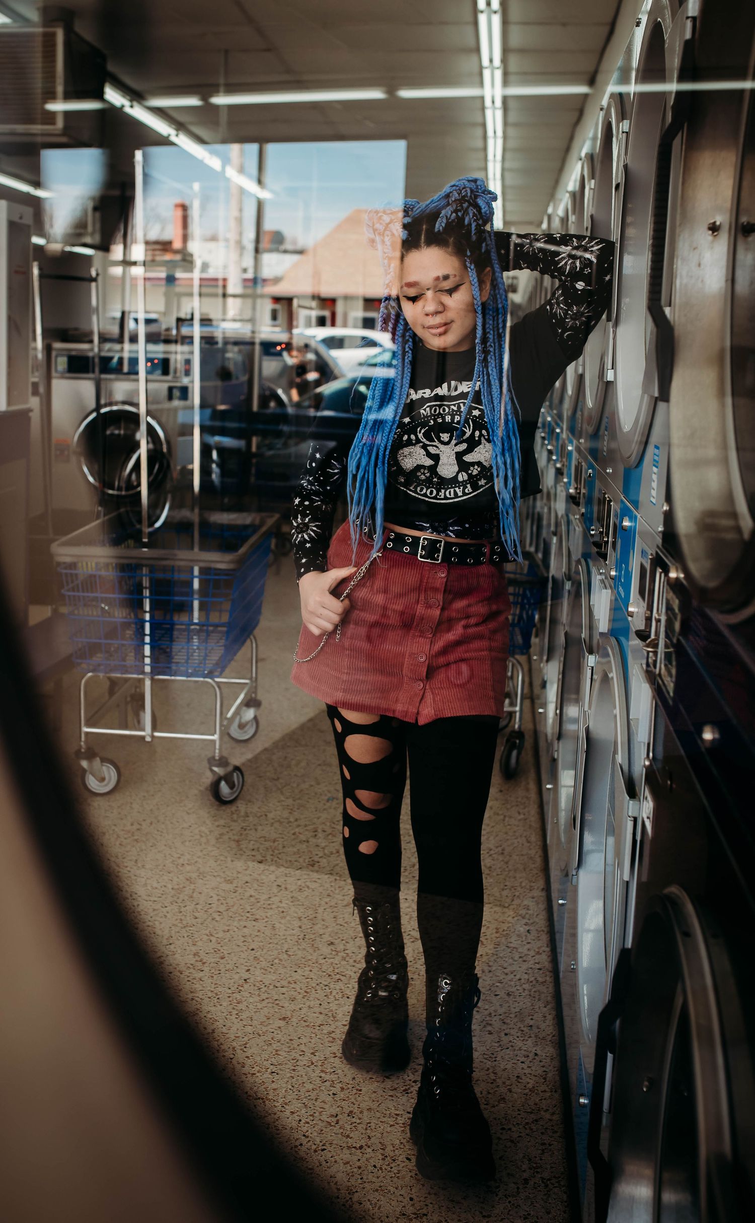Person in ripped jeans and boots standing between rows of commercial washing machines.