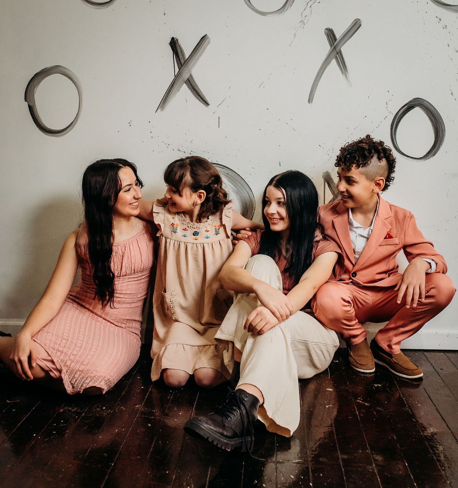 A group sits together on a wooden floor against a wall with X and O decorations.