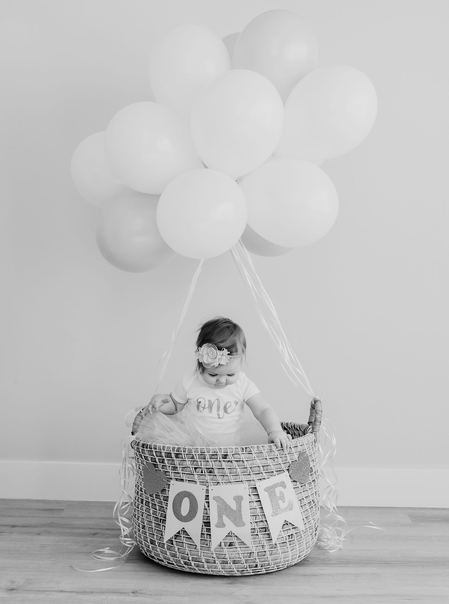 A black and white photo of a birthday setup with white balloons and a decorated basket.