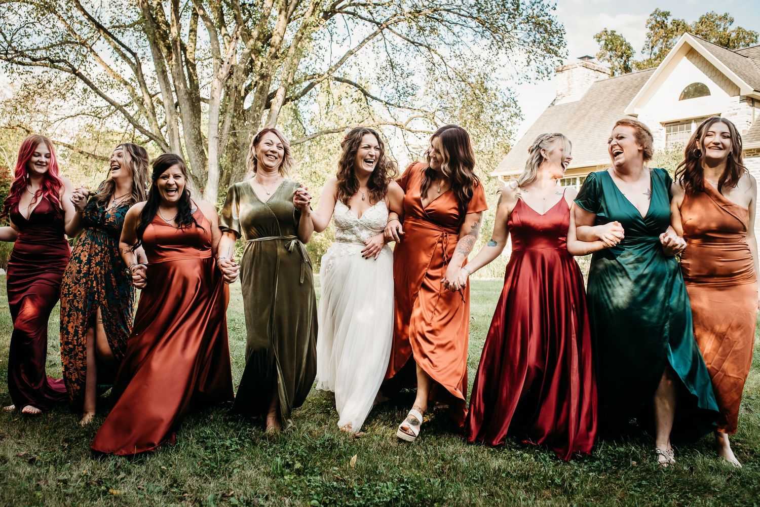 Wedding party in burgundy and rust-colored dresses posed together outdoors.