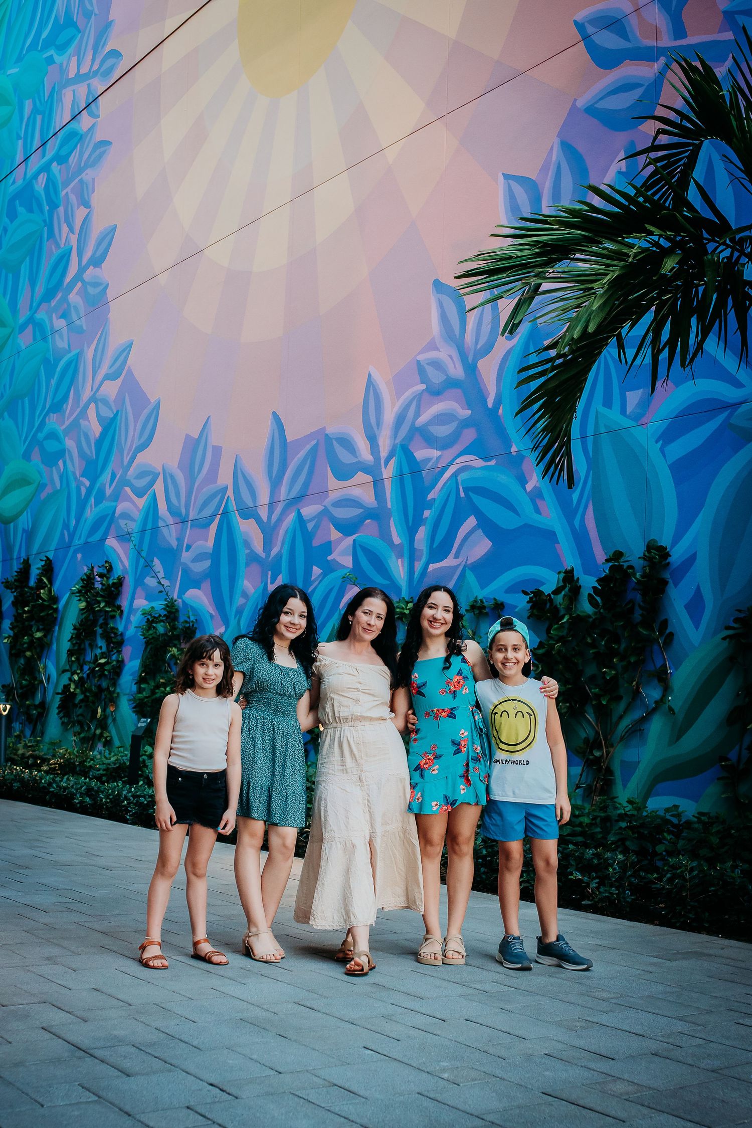 Group photo of five people standing against colorful mural with palm trees and geometric patterns.