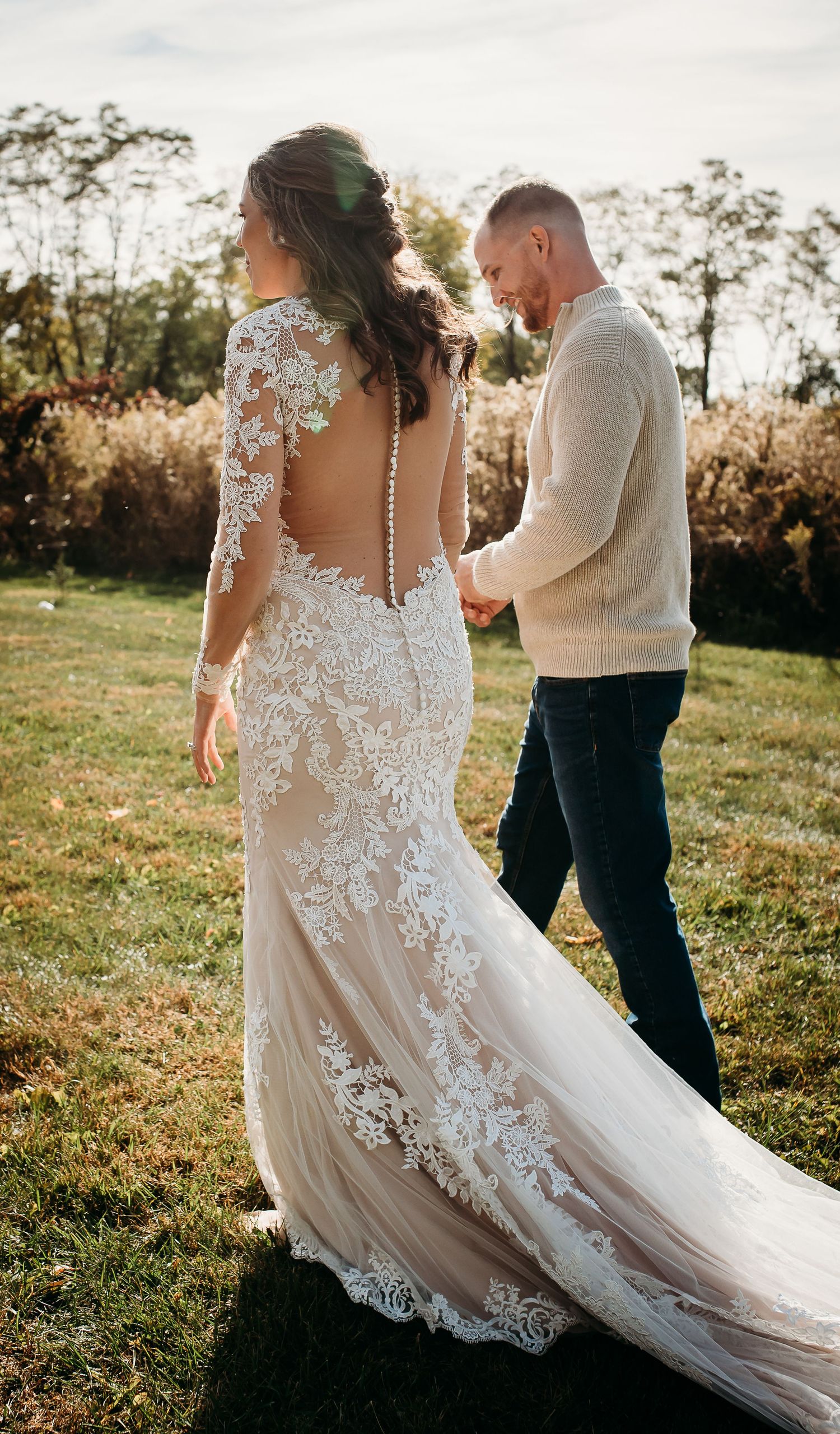 Intricate lace details of a wedding dress flow in the golden sunlight during an outdoor celebration.