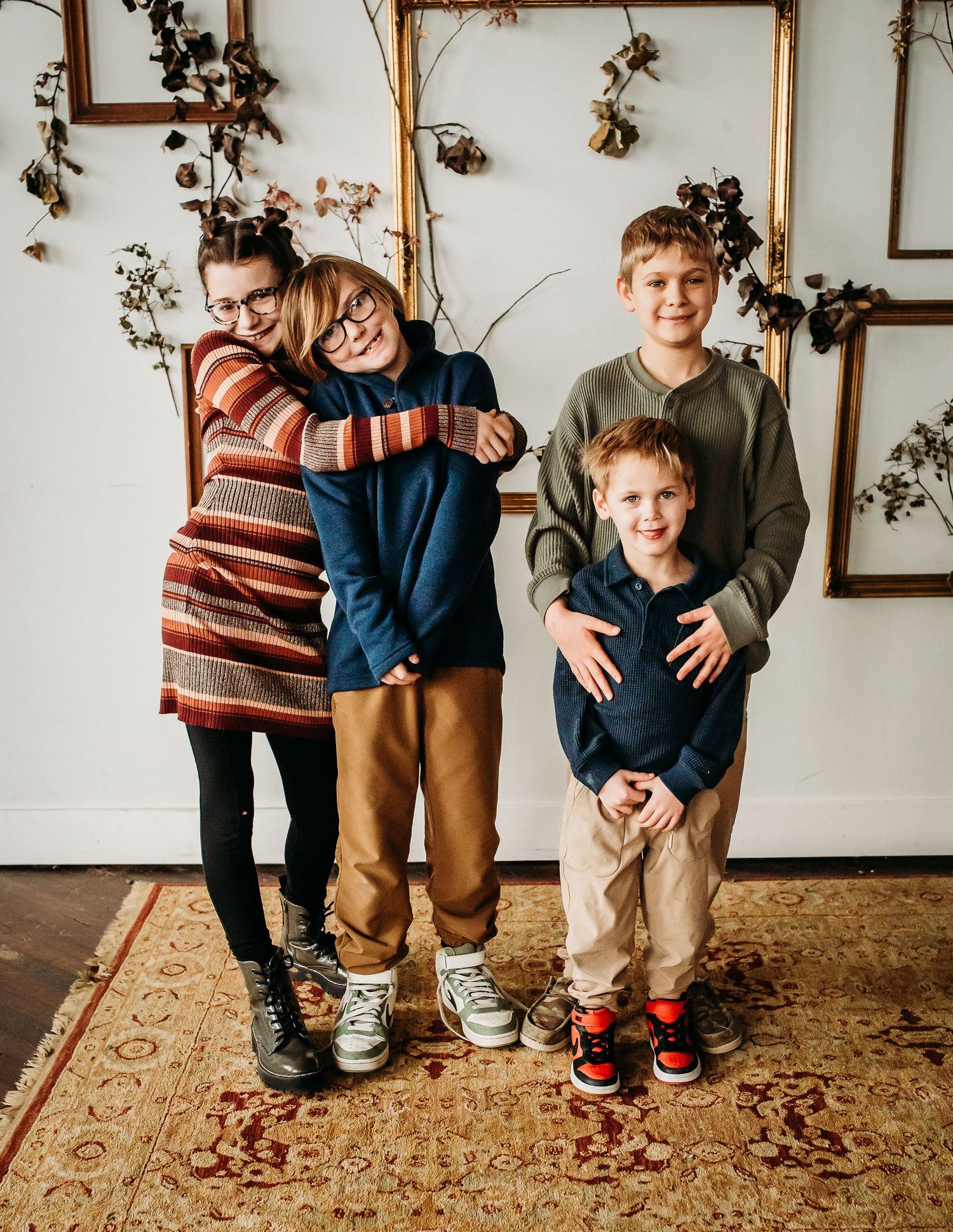 A family group hugs and poses playfully against wall with dried floral decorations.