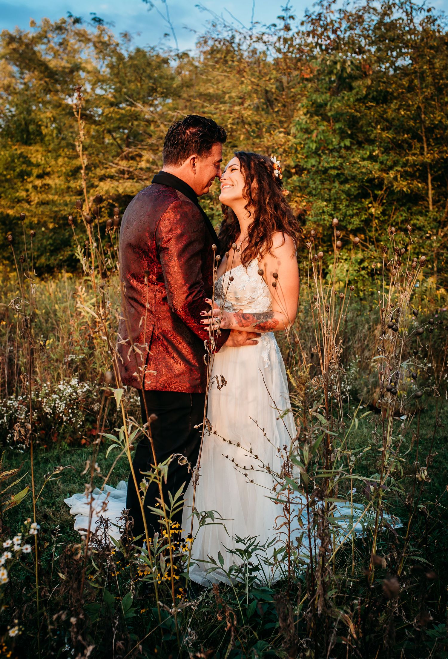 Sunset wedding photos in tall wildflowers with couple in white gown and burgundy suit.