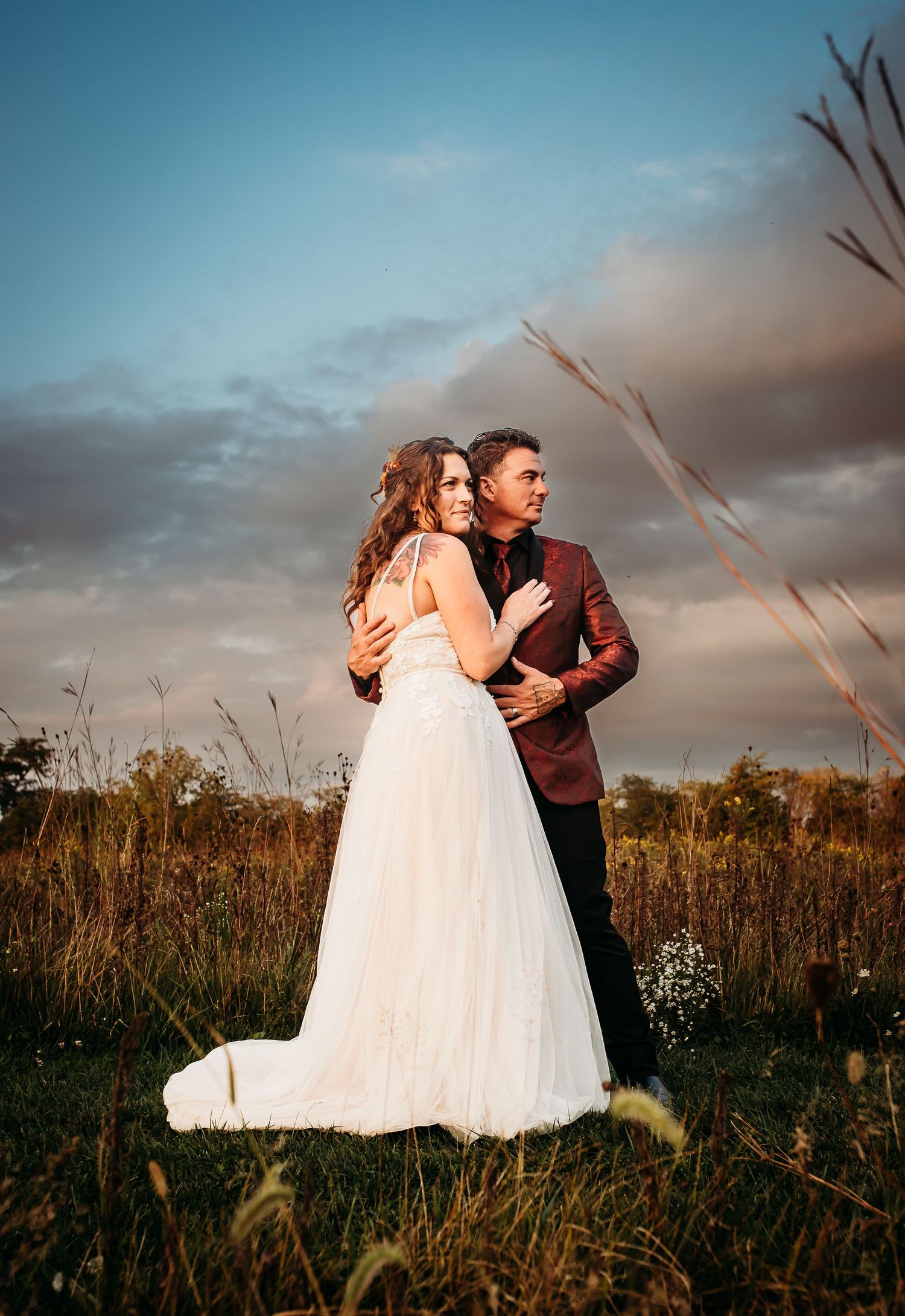 A couple in formal attire shares an intimate moment in a field at dusk.