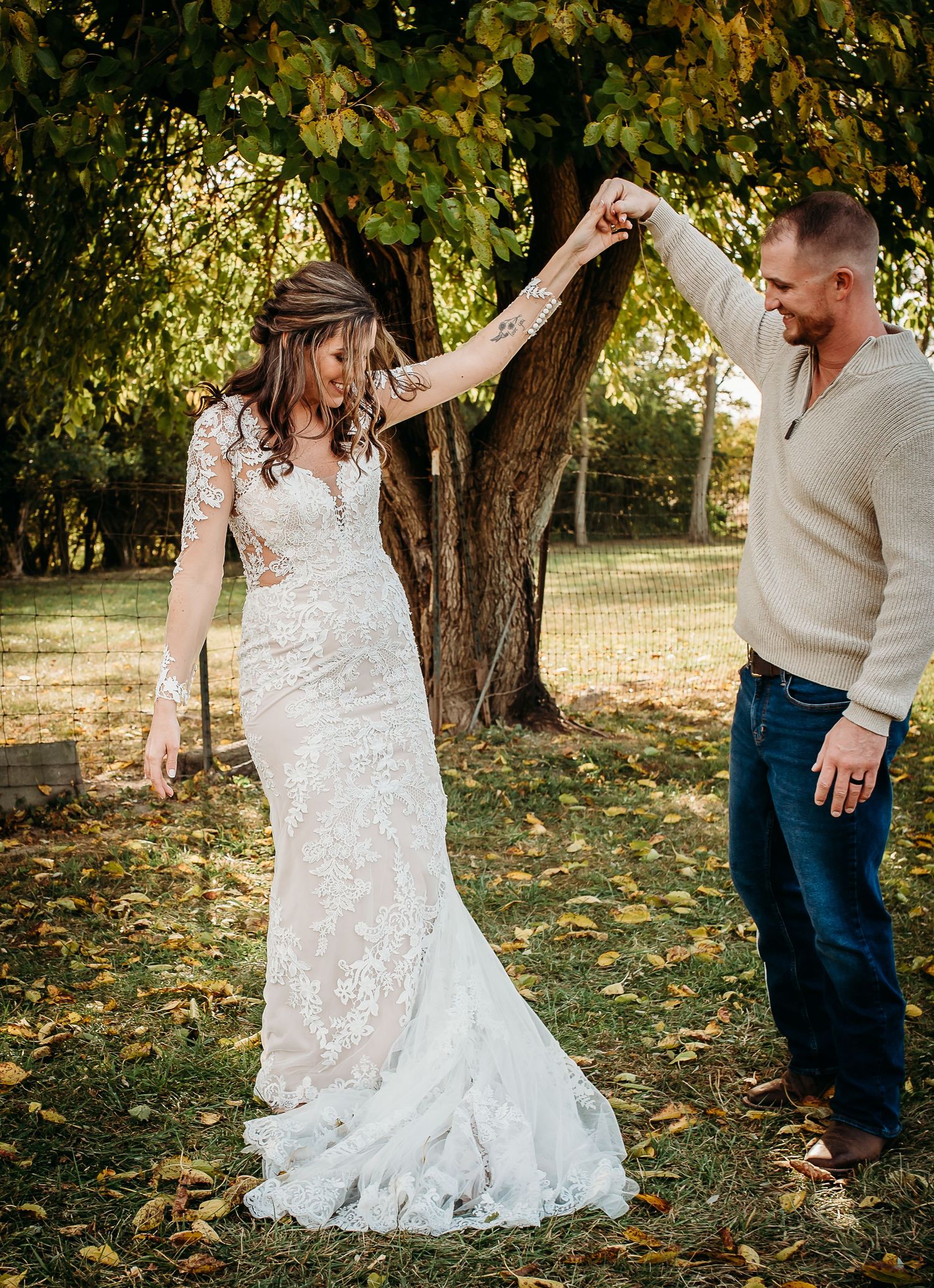 Dancing and twirling in an elaborate lace wedding dress during an autumn outdoor celebration.