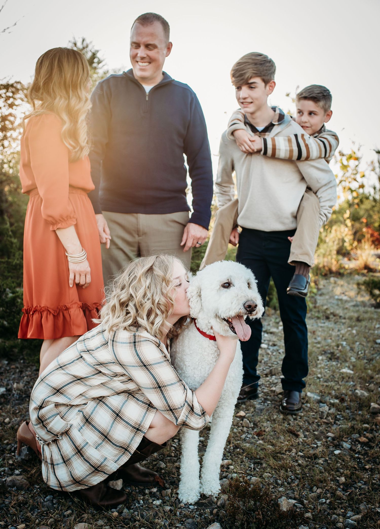A family gathering outdoors with their white dog on rocky terrain at sunset.