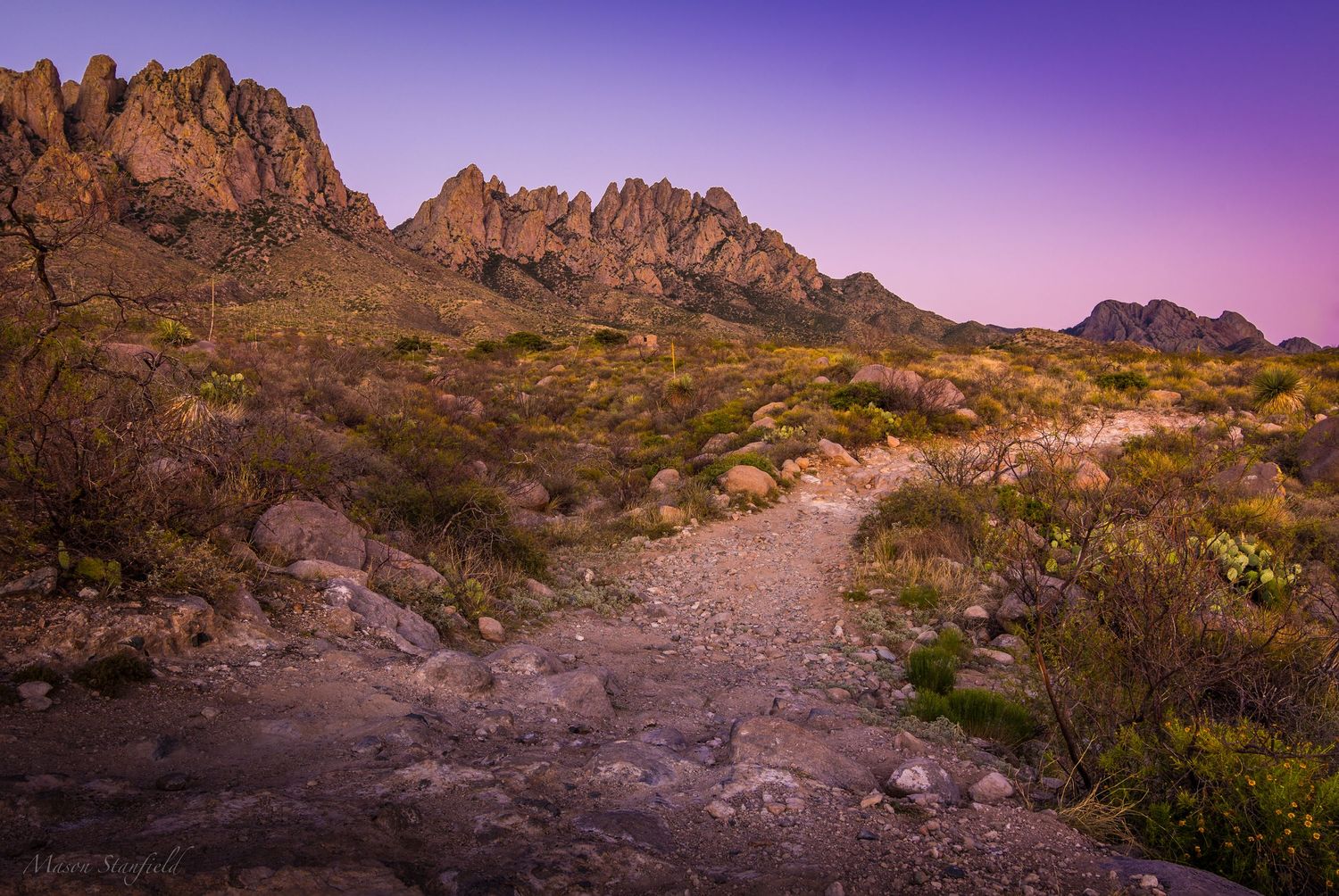 Rocky mountain trail winding through desert landscape under purple twilight sky.