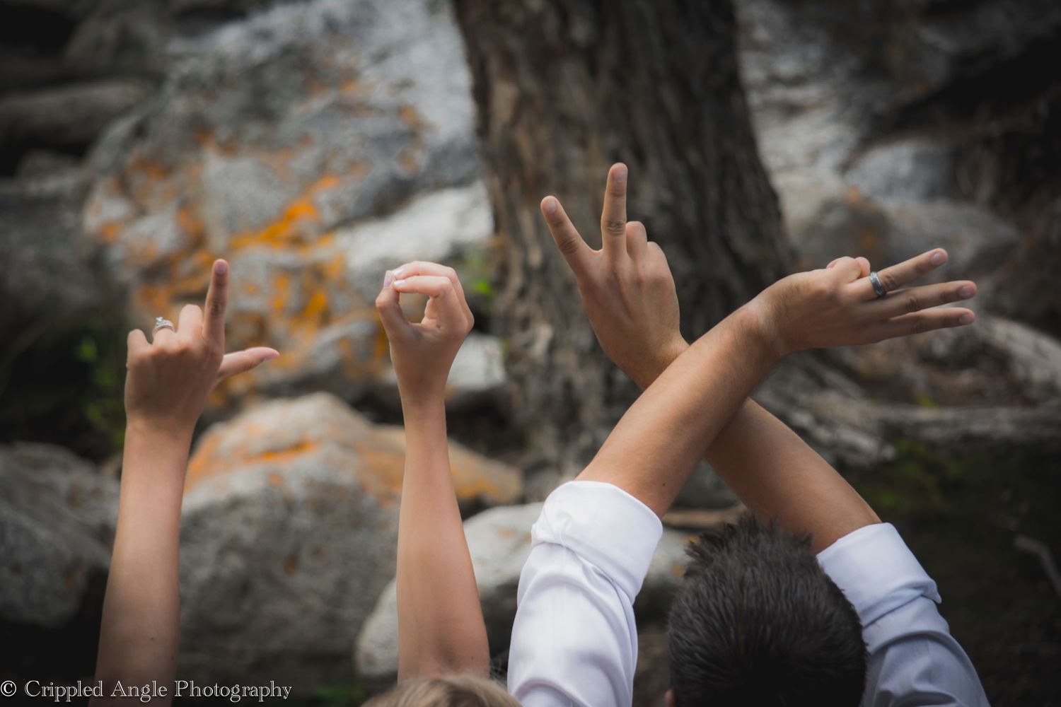 Raised hands making LOVE signs against rocky river backdrop.