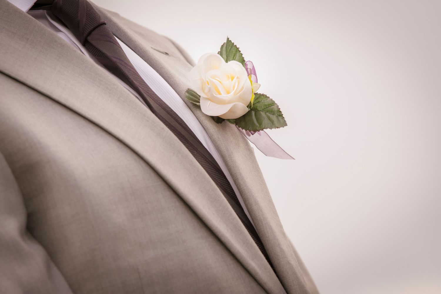 Close-up of a white rose boutonniere pinned to a light gray suit jacket.