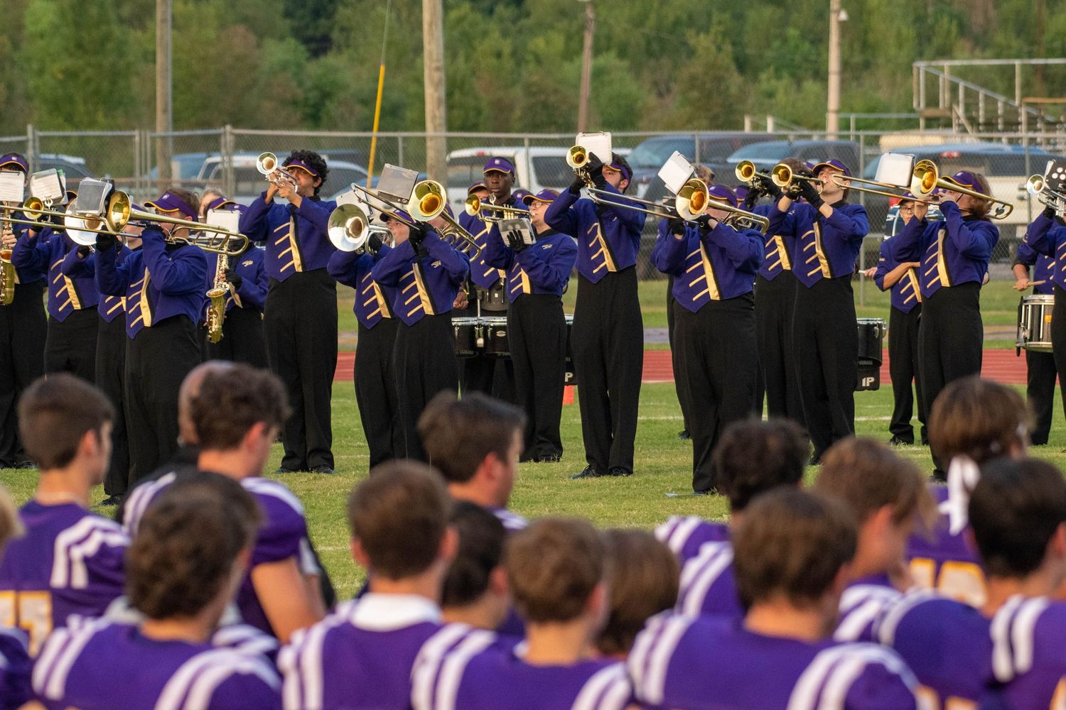 High school marching band in purple uniforms performing on football field.