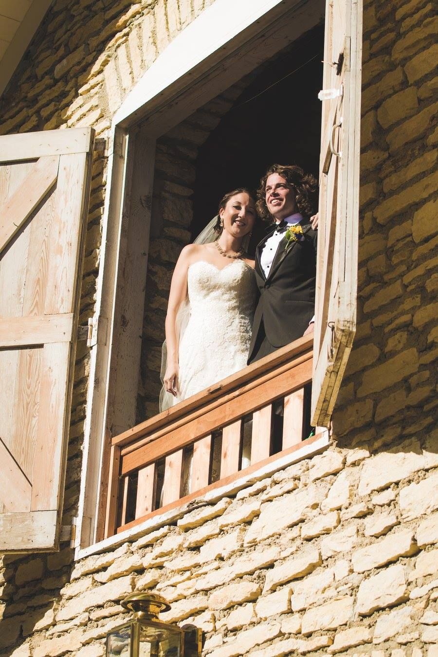 A couple poses in the doorway of a historic stone building with rustic wooden doors.