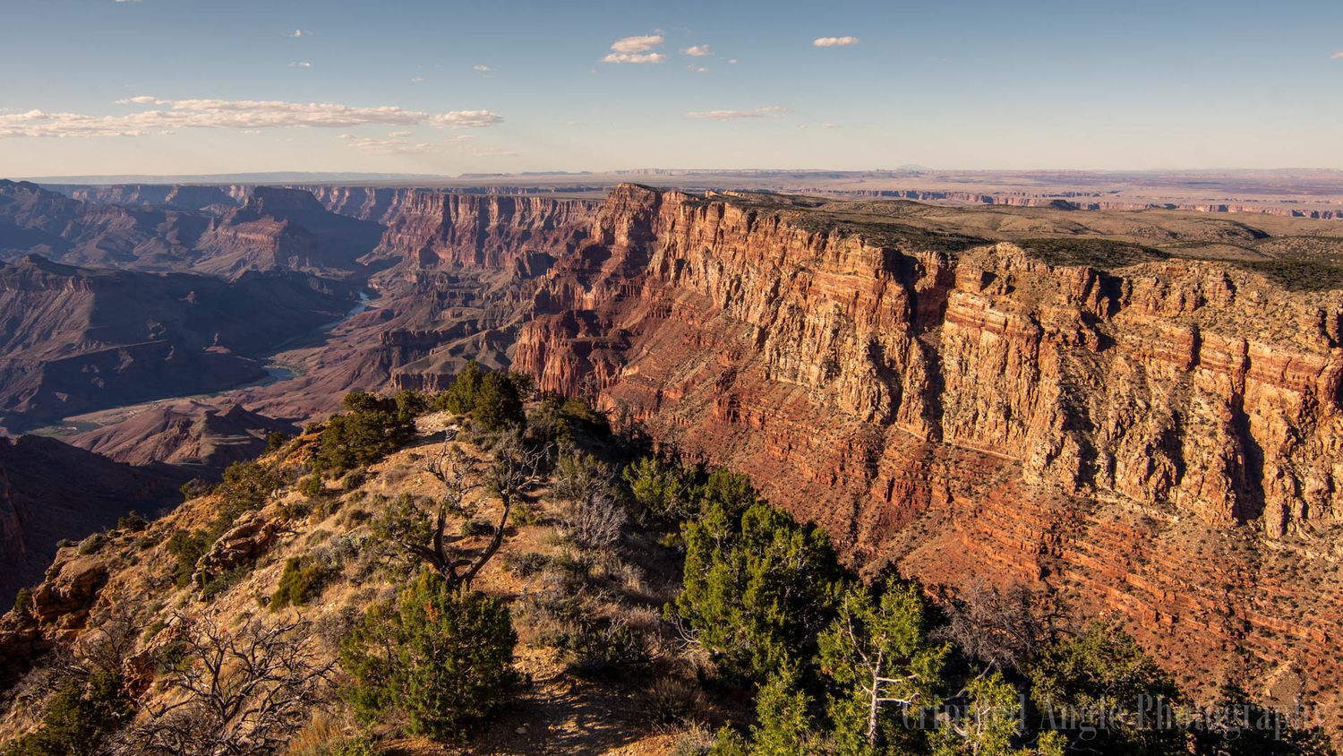 Sweeping view of the Grand Canyon's red rock cliffs and deep gorges under a bright blue sky.